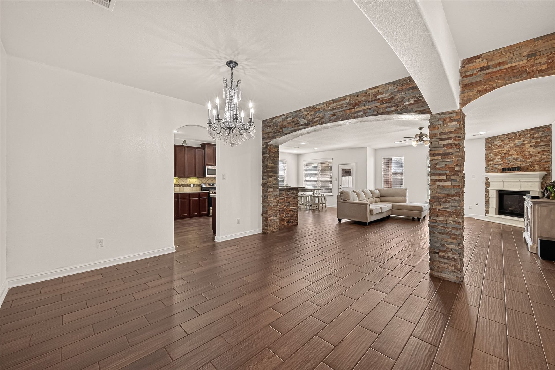 2826 Verdant Spring Trail, Katy, TX 77493 Elegant formal dining room flows into the living area, featuring wood-look tile flooring, a stone fireplace, and a stylish chandelier, with seamless access to a modern kitchen with rich cabinetry.