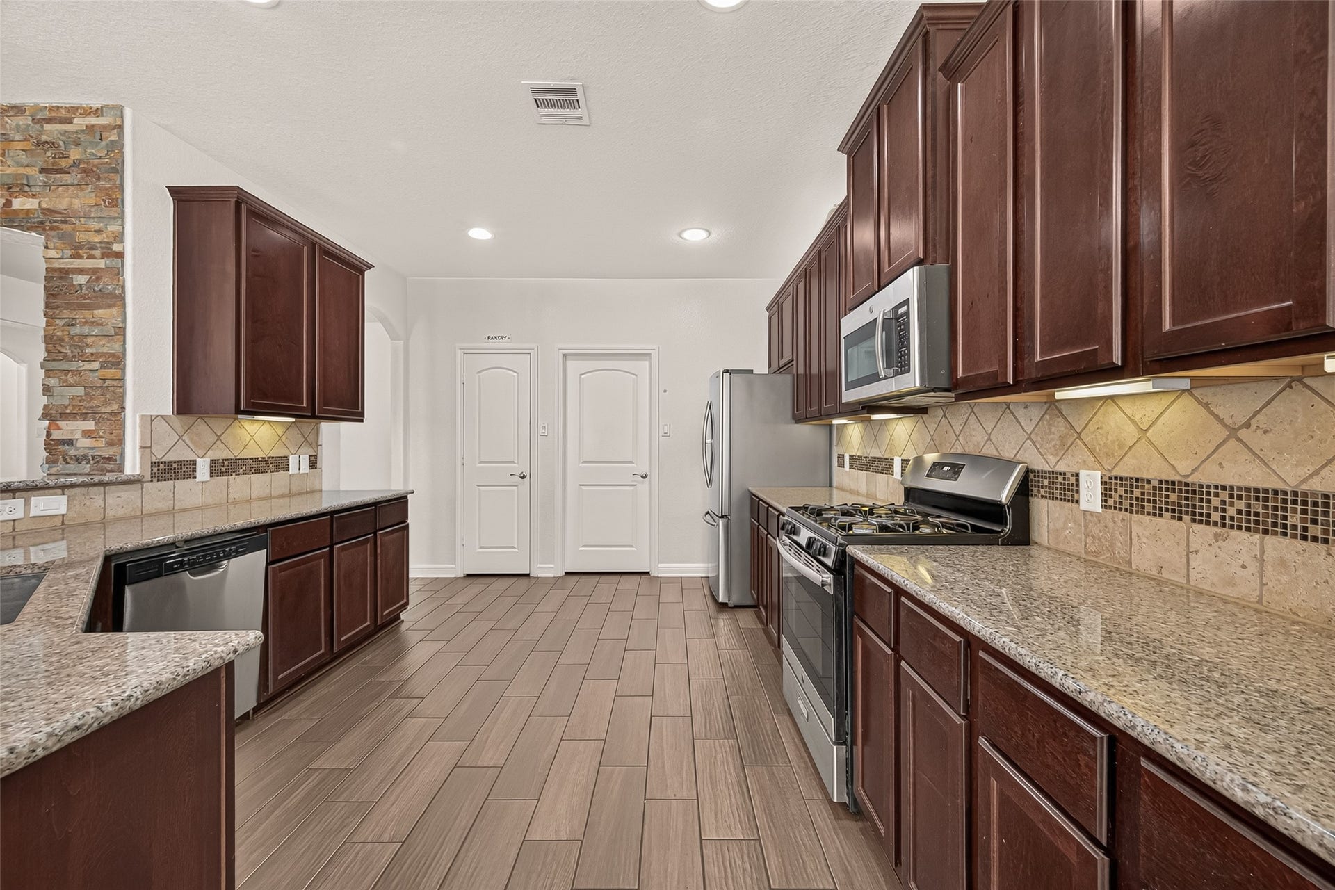 2826 Verdant Spring Trail, Katy, TX 77493 Spacious kitchen with rich wood cabinetry, sleek granite countertops, and modern stainless steel appliances, accented by a stylish tile backsplash and flooring.