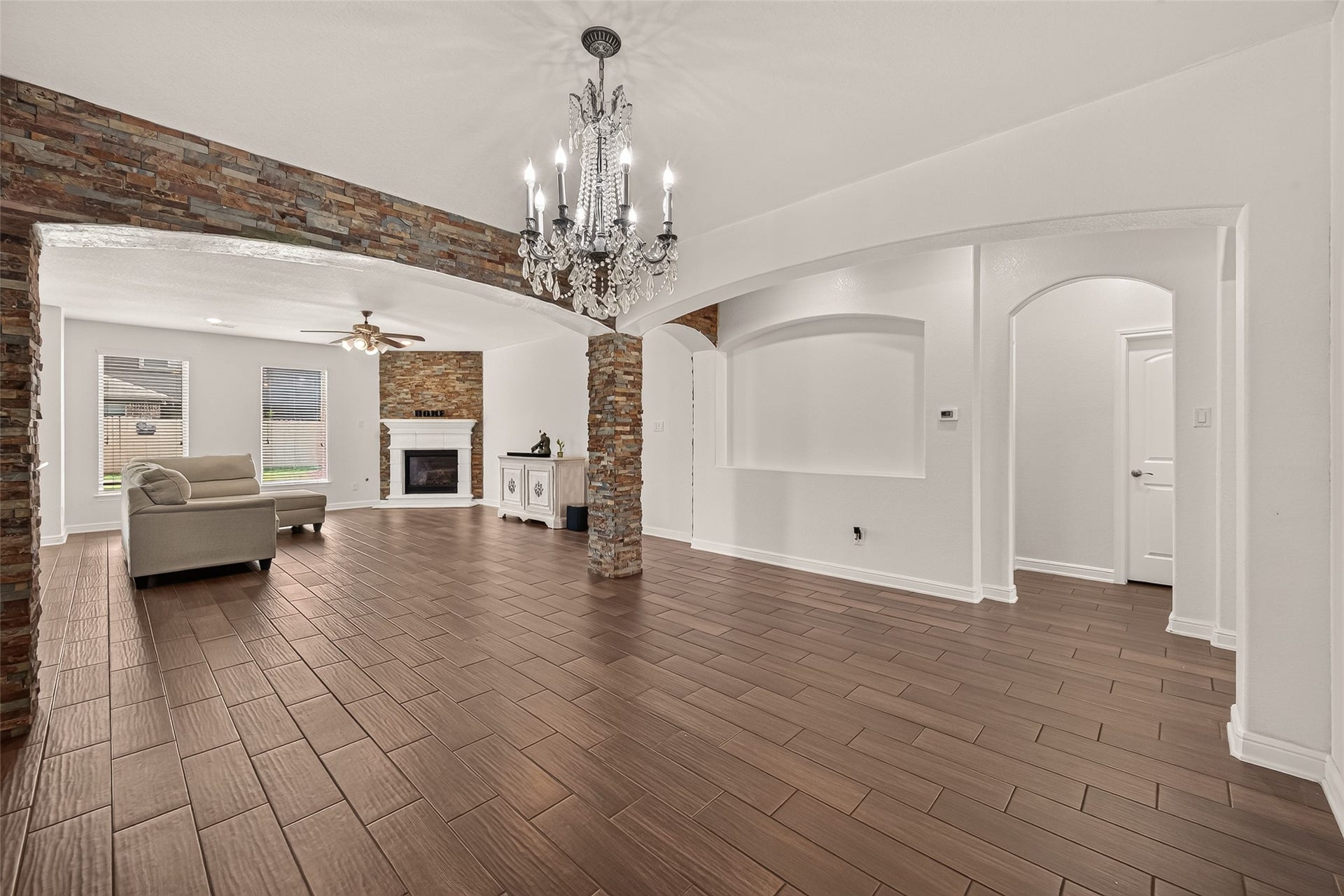 2826 Verdant Spring Trail, Katy, TX 77493 Elegant living space featuring rich wood-like flooring, a cozy fireplace, and a stunning chandelier. The room is accentuated by stone columns and archways, offering a blend of modern and classic charm.