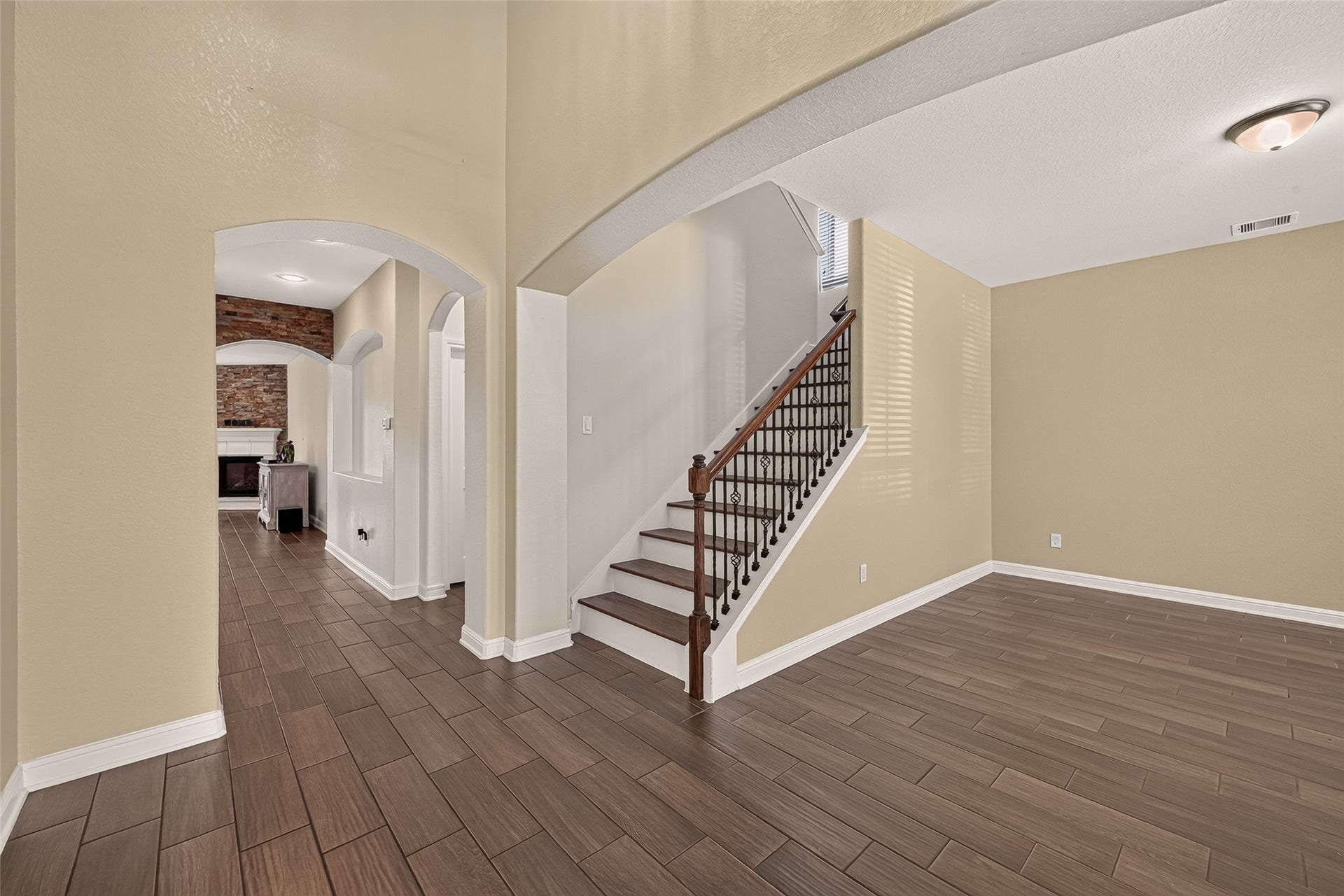 2826 Verdant Spring Trail, Katy, TX 77493 Elegant entryway featuring rich wood-look tile flooring and graceful archways, leading to a charming staircase with decorative iron balusters.