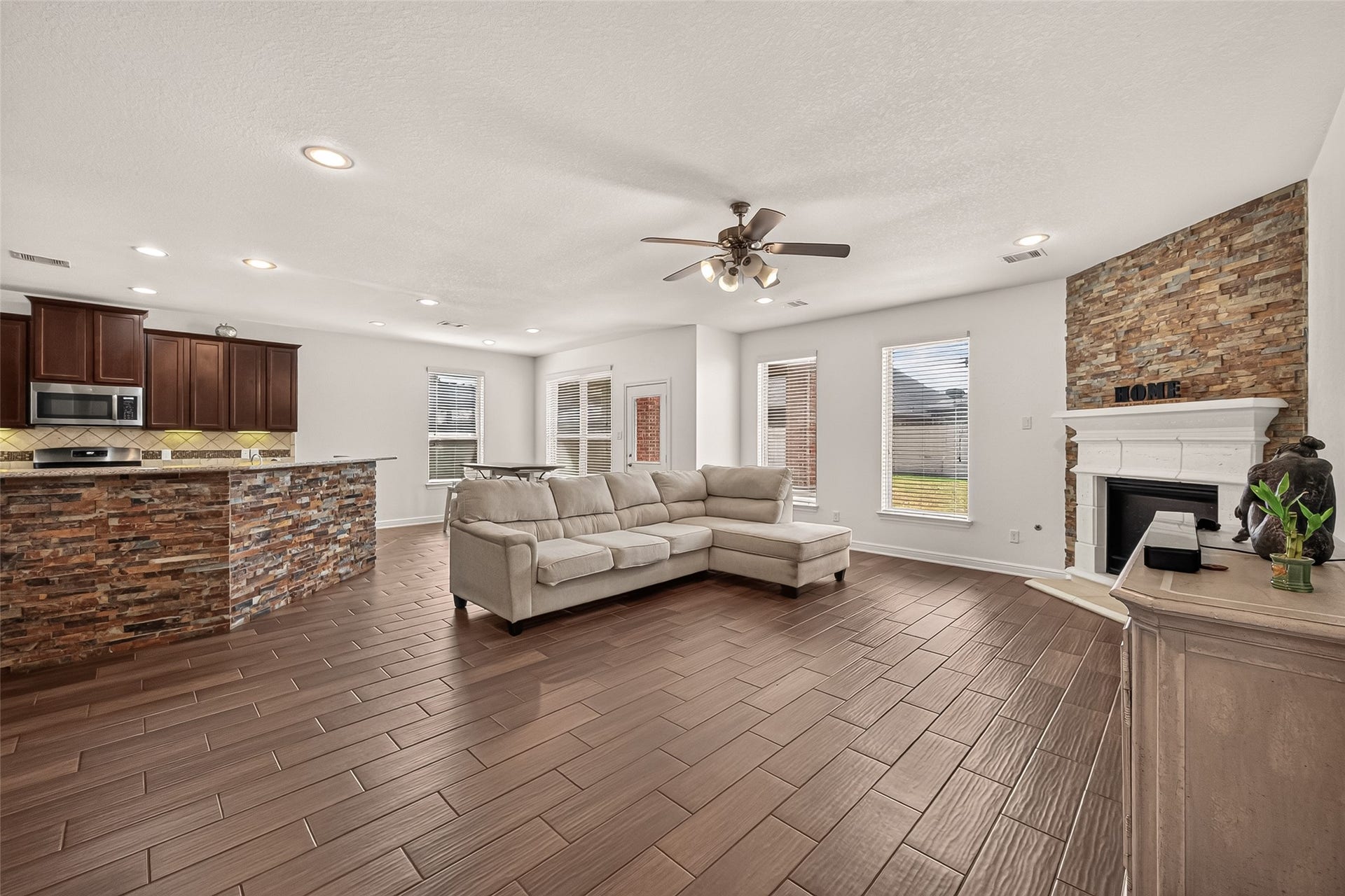2826 Verdant Spring Trail, Katy, TX 77493 Spacious open concept living area with a cozy stone fireplace, elegant wood-look tile flooring, and a modern kitchen featuring rich cabinetry and a stone-accented breakfast bar.