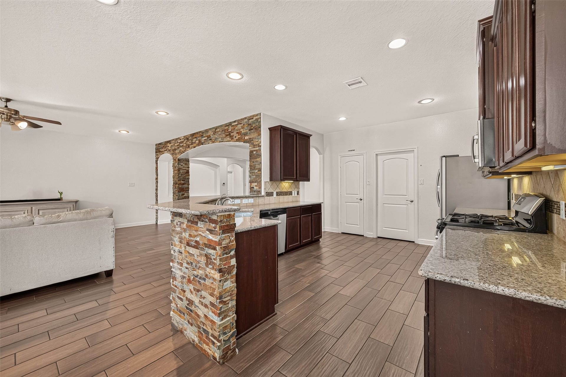 2826 Verdant Spring Trail, Katy, TX 77493 Spacious modern kitchen featuring dark wood cabinetry, sleek granite countertops, and a striking stone accent wall, flowing seamlessly into a cozy living room.