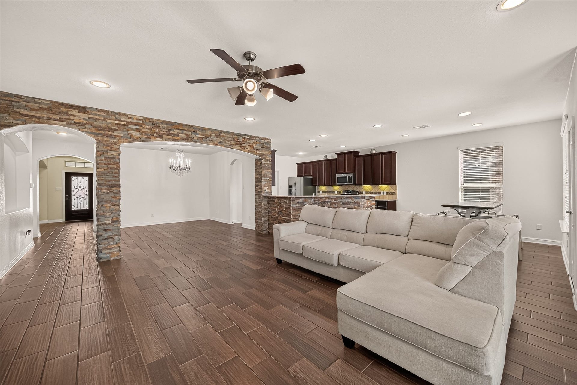 2826 Verdant Spring Trail, Katy, TX 77493 Spacious open-concept living area features elegant tile flooring, a modern ceiling fan, and a cozy sectional. The room flows seamlessly into a stylish kitchen with dark wood cabinetry and stainless steel appliances, while stone archways add a touch of rustic charm.