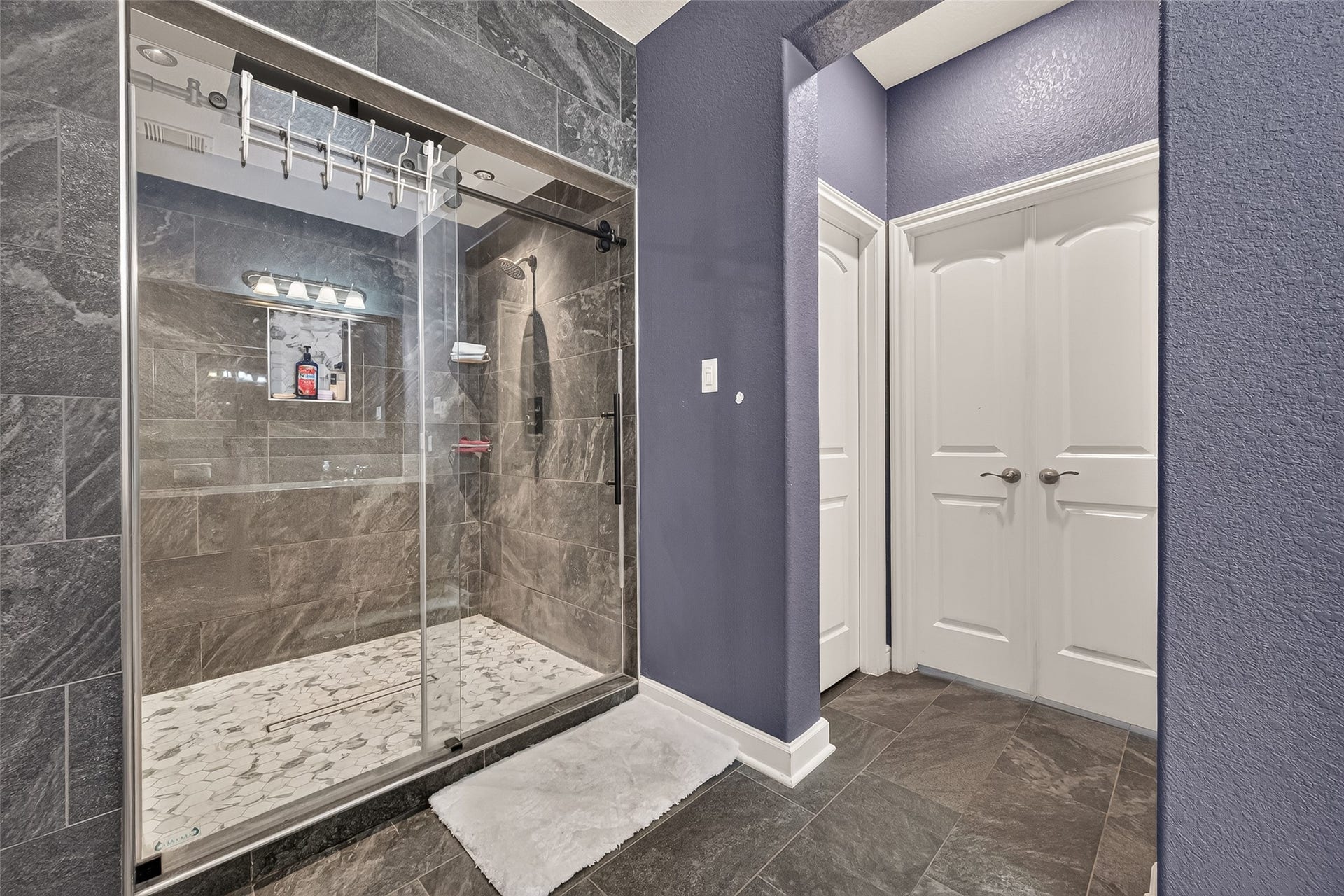 2826 Verdant Spring Trail, Katy, TX 77493 Refined primary bathroom featuring a spacious glass-enclosed shower with sleek dark tilework and contemporary fixtures, complemented by elegant double doors opening to an expansive walk-in closet.