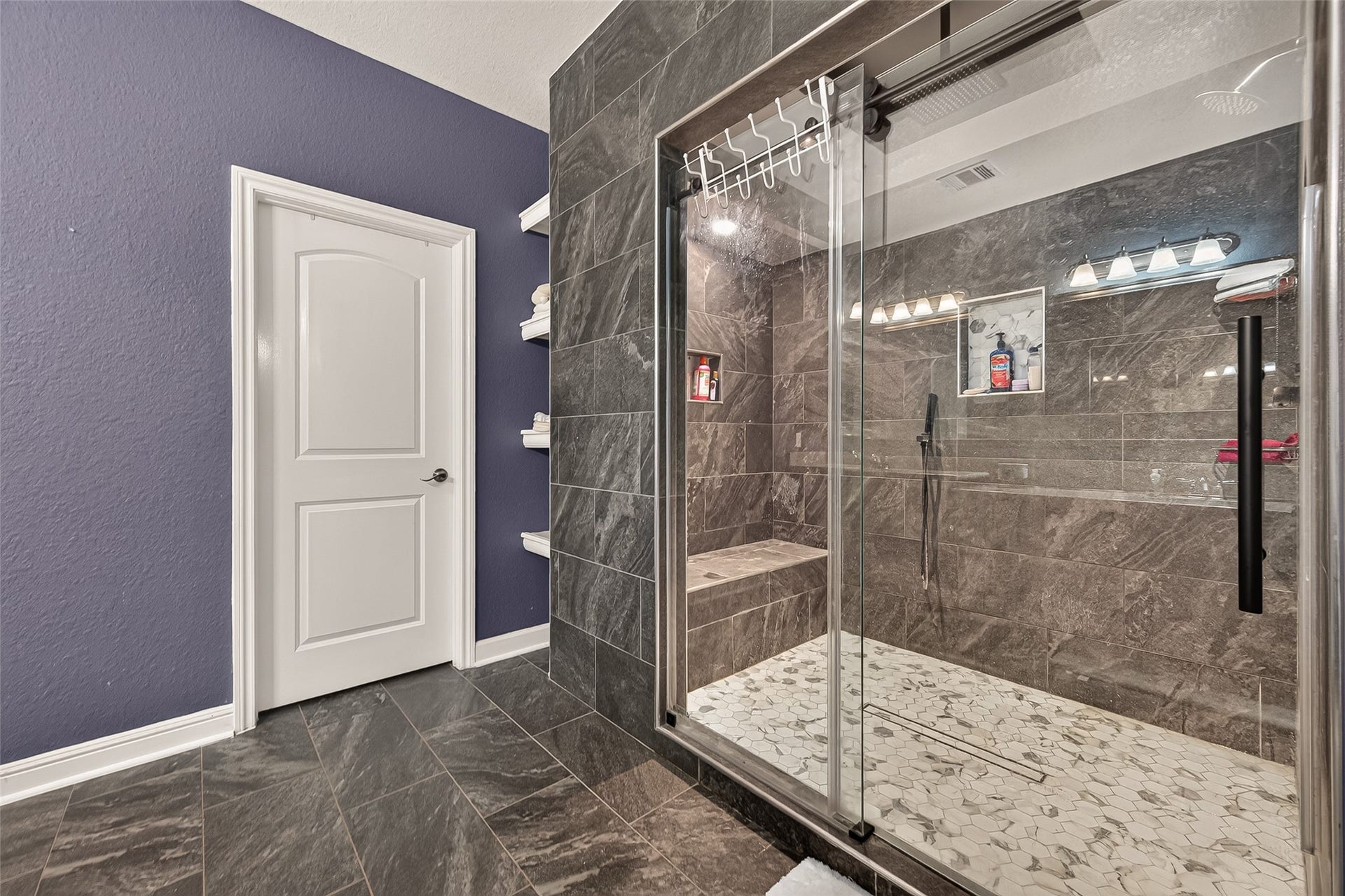 2826 Verdant Spring Trail, Katy, TX 77493 Luxurious bathroom featuring an expansive walk-in shower with frameless glass doors and sophisticated stone tilework, accented by a rich purple wall and convenient built-in shelving.