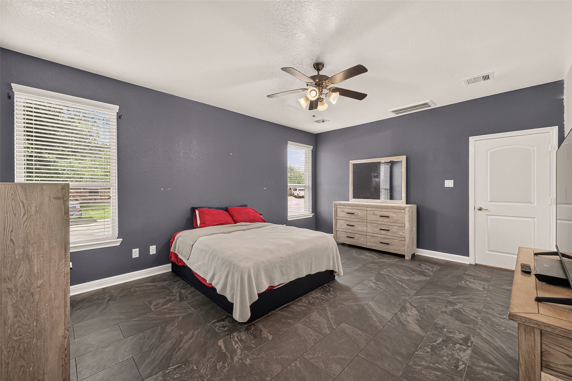 2826 Verdant Spring Trail, Katy, TX 77493 Spacious primary suite featuring sleek tile flooring, sophisticated dark walls, dual windows with abundant natural light, and a modern ceiling fan.