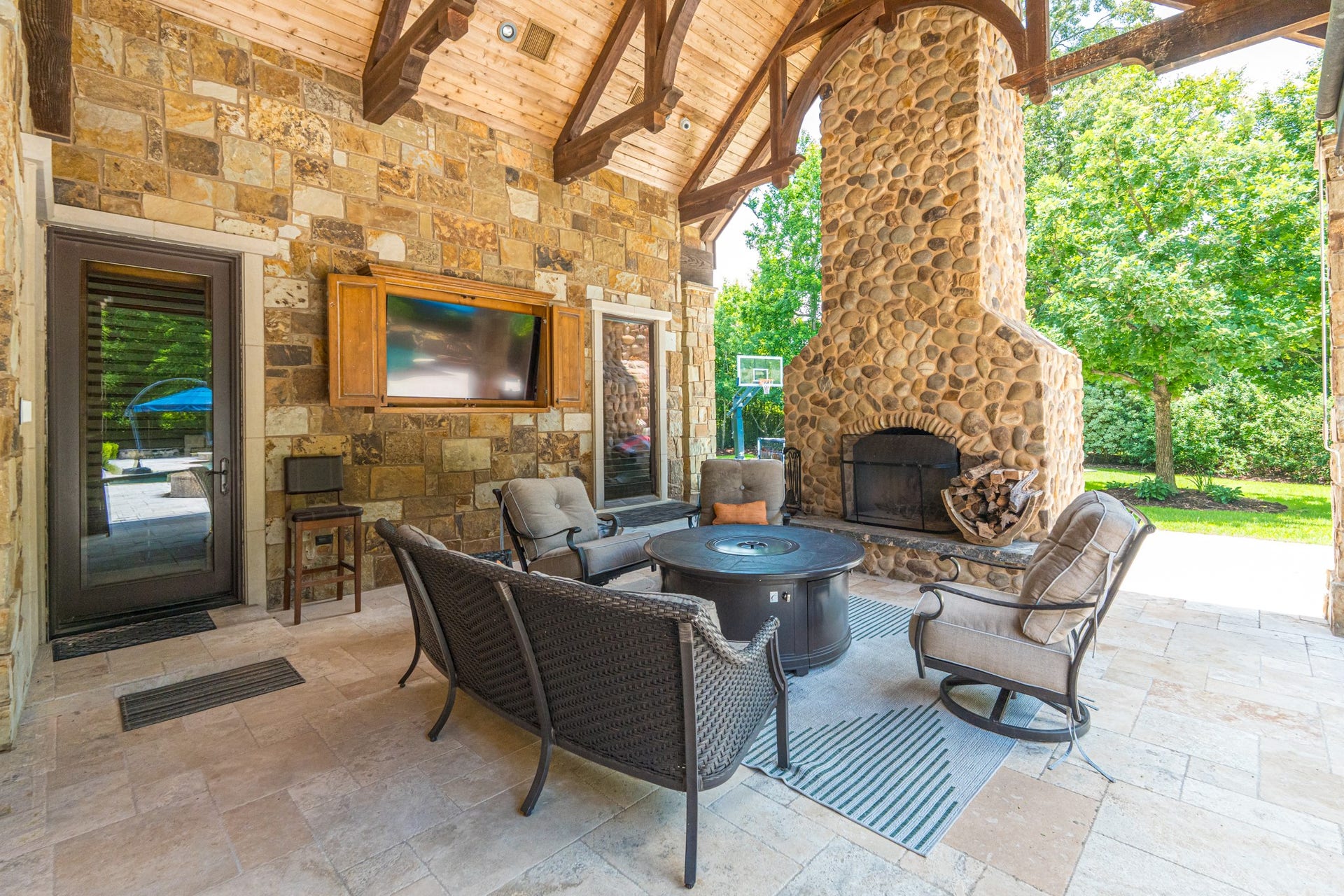 247 S Fazio Way, Spring, TX 77389 Designed for year-round enjoyment, this spacious outdoor living room features a floor-to-ceiling stone fireplace, mounted TV, soaring wood-beamed ceilings, and comfortable gathering spaces overlooking the resort-style backyard.