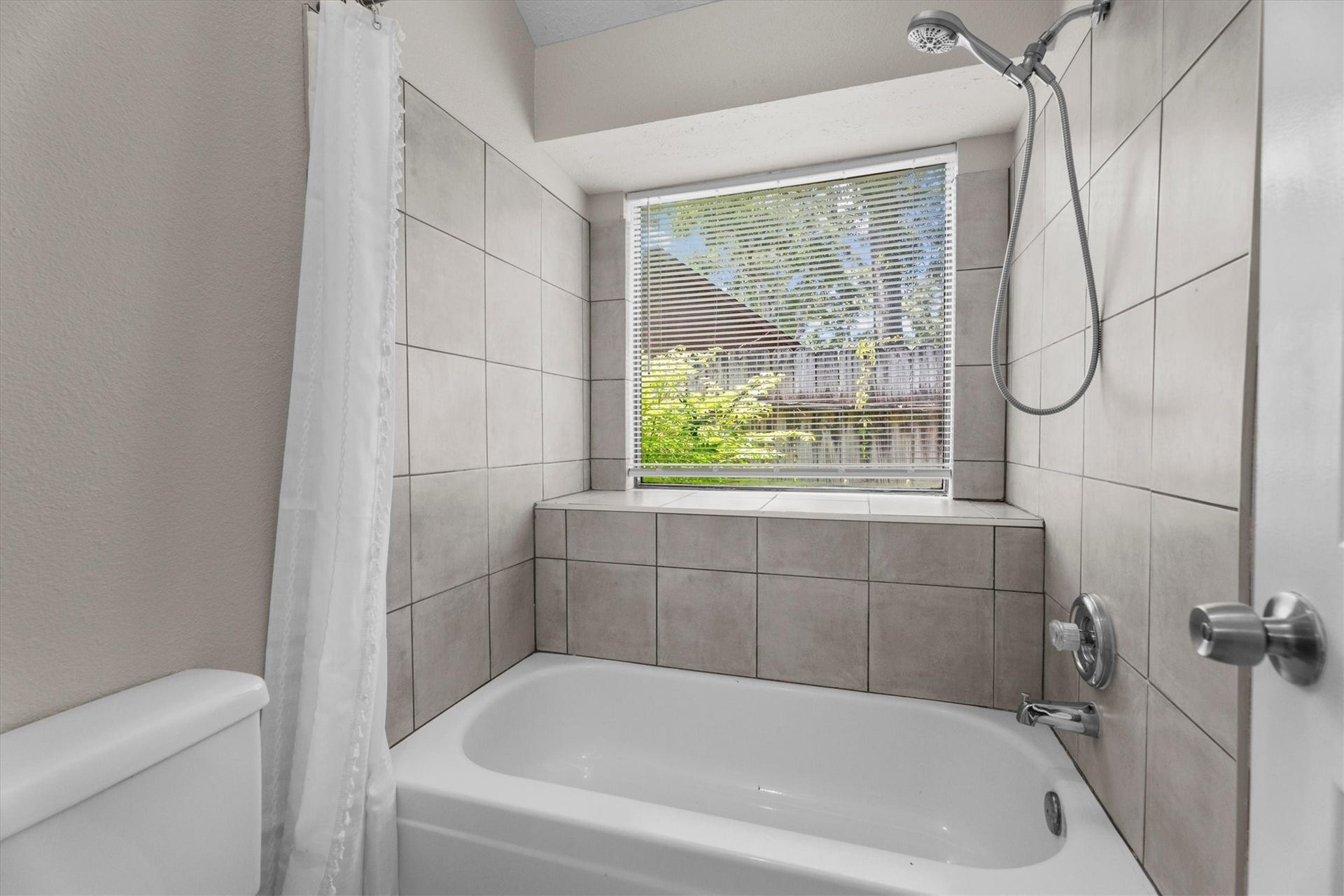 A tiled tub and shower surround includes a window that brings in natural light and adds a bright touch to the space.