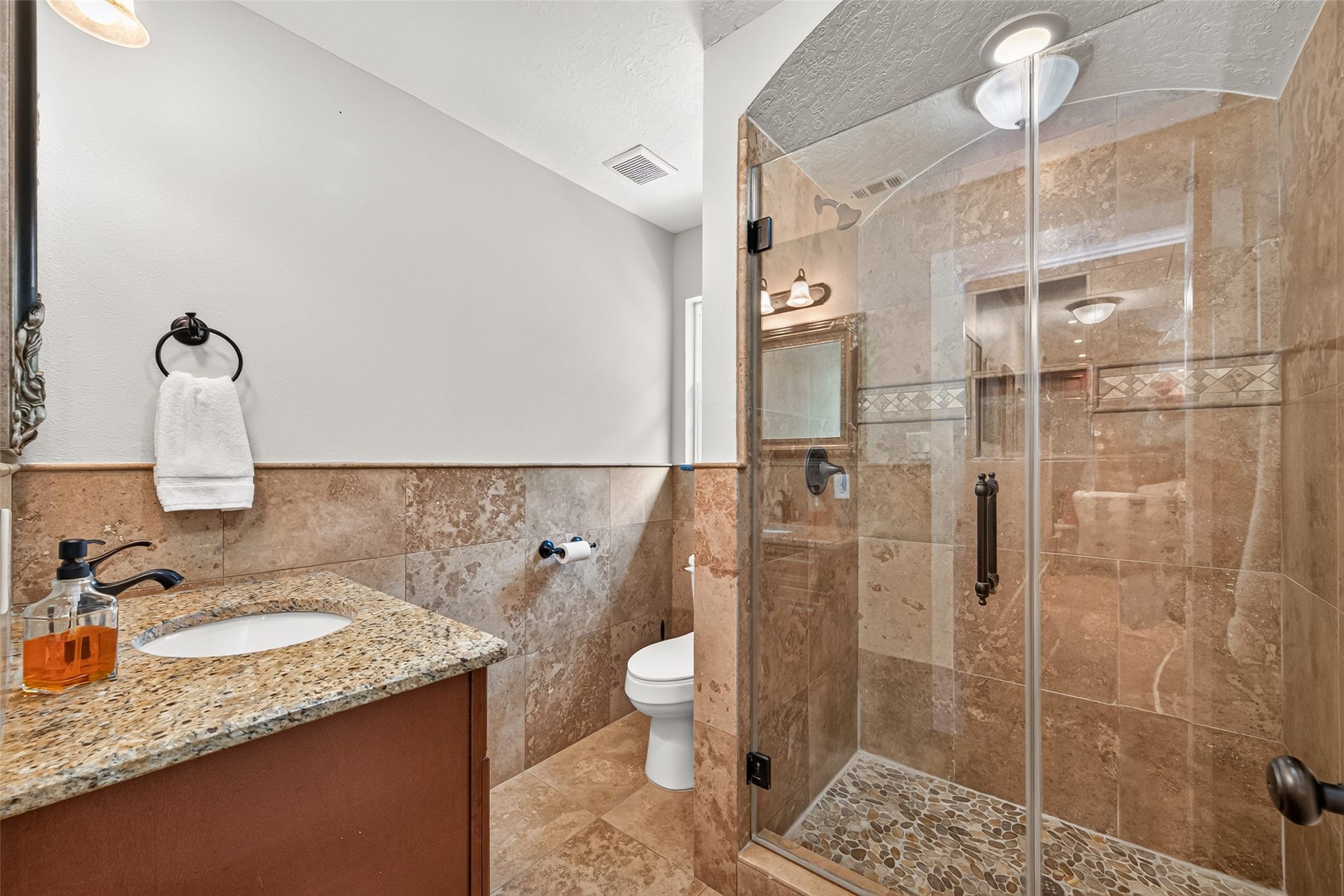 Secondary bathroom features a granite vanity and tiled walk-in shower with frameless glass enclosure and decorative accents.