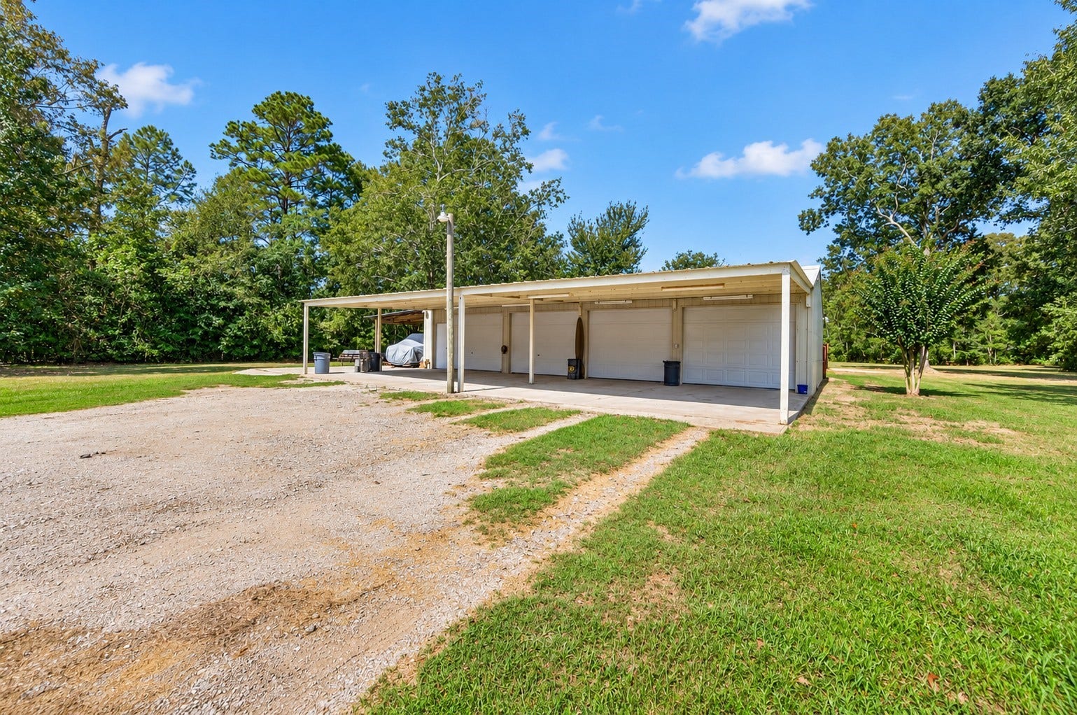4-car bay shop with covered parking/storage and a wide gravel drive providing easy vehicle and equipment access