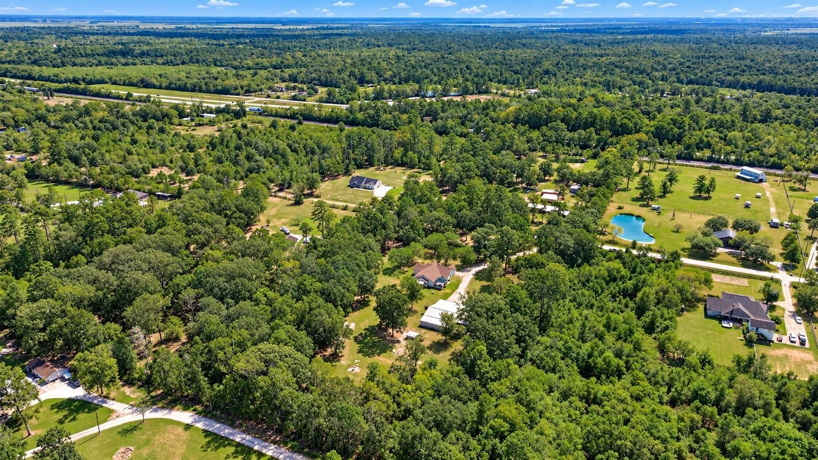 Aerial view showcasing the propertys peaceful setting surrounded by mature trees and neighboring acreage.