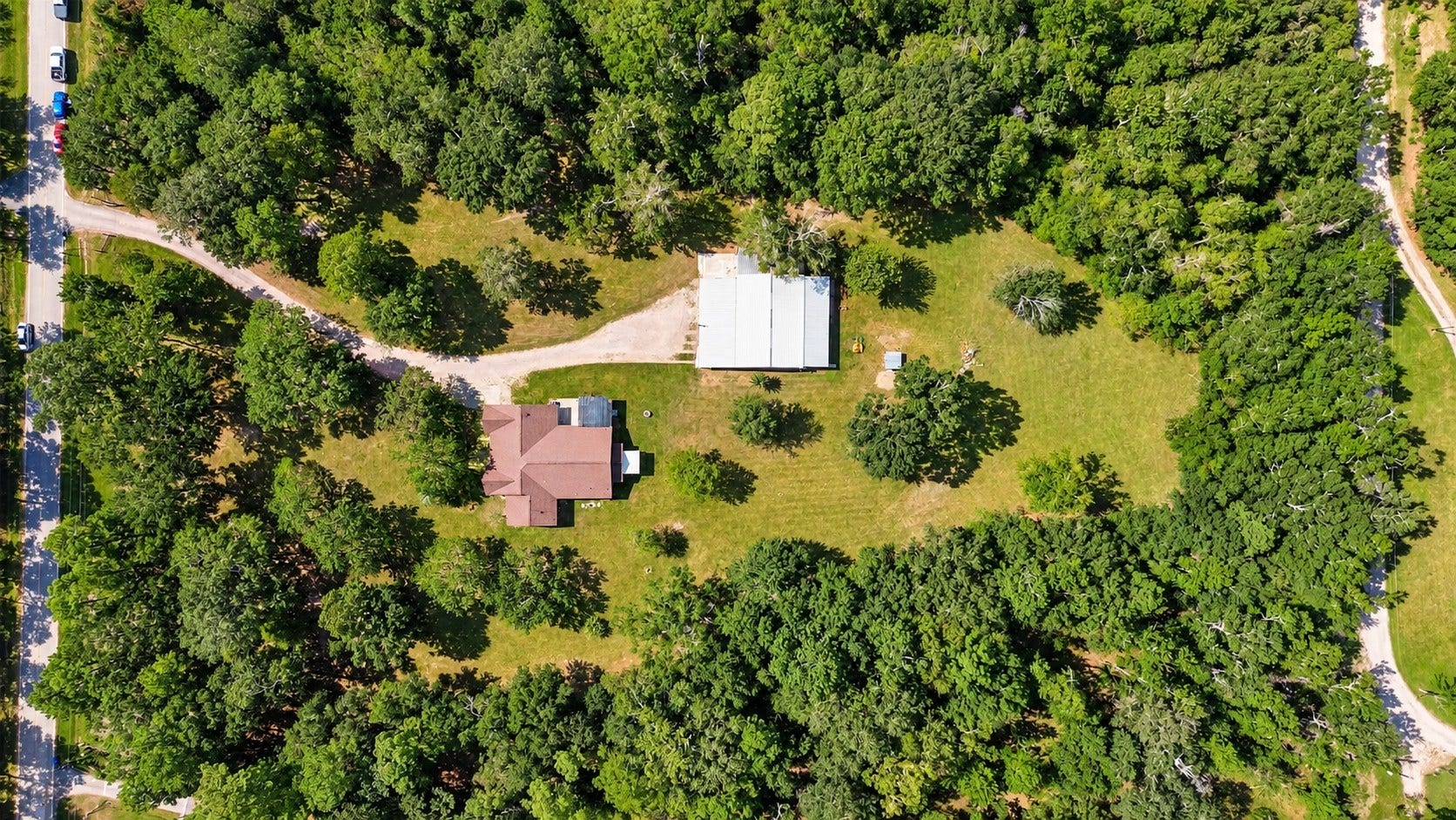 Overhead aerial showcasing the home, large shop, expansive open space, and mature trees throughout the property.