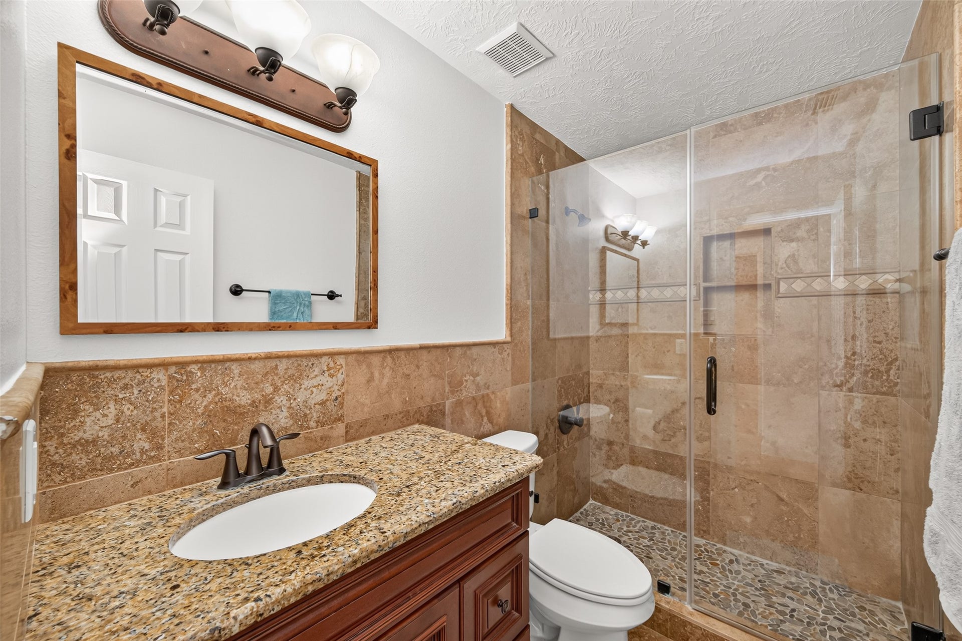 Additional secondary bathroom features a granite vanity and tiled walk-in shower with frameless glass enclosure and decorative accents.