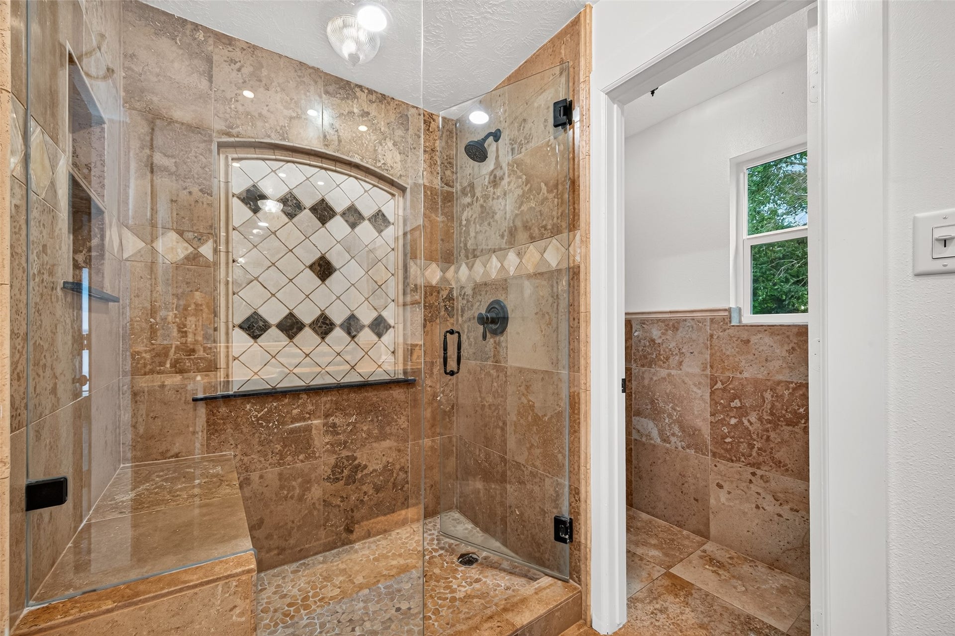 Primary en-suite features a spacious walk-in shower with frameless glass, floor-to-ceiling tile, built-in bench and decorative tile accents.