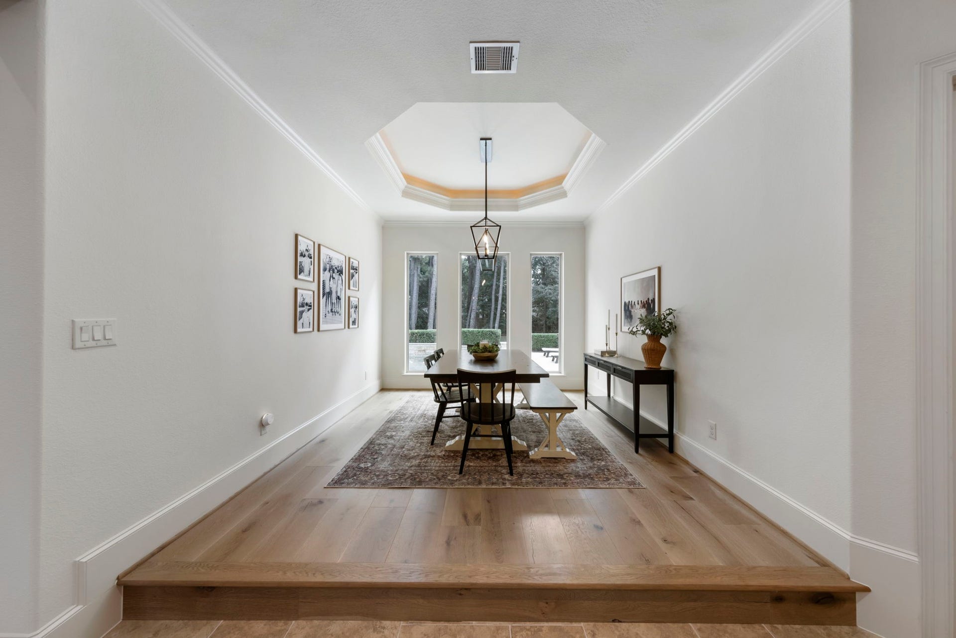 Set on a striking raised wood-plank platform beneath an octagonal tray ceiling, this dining space is framed by wall-to-wall windows overlooking the backyard.