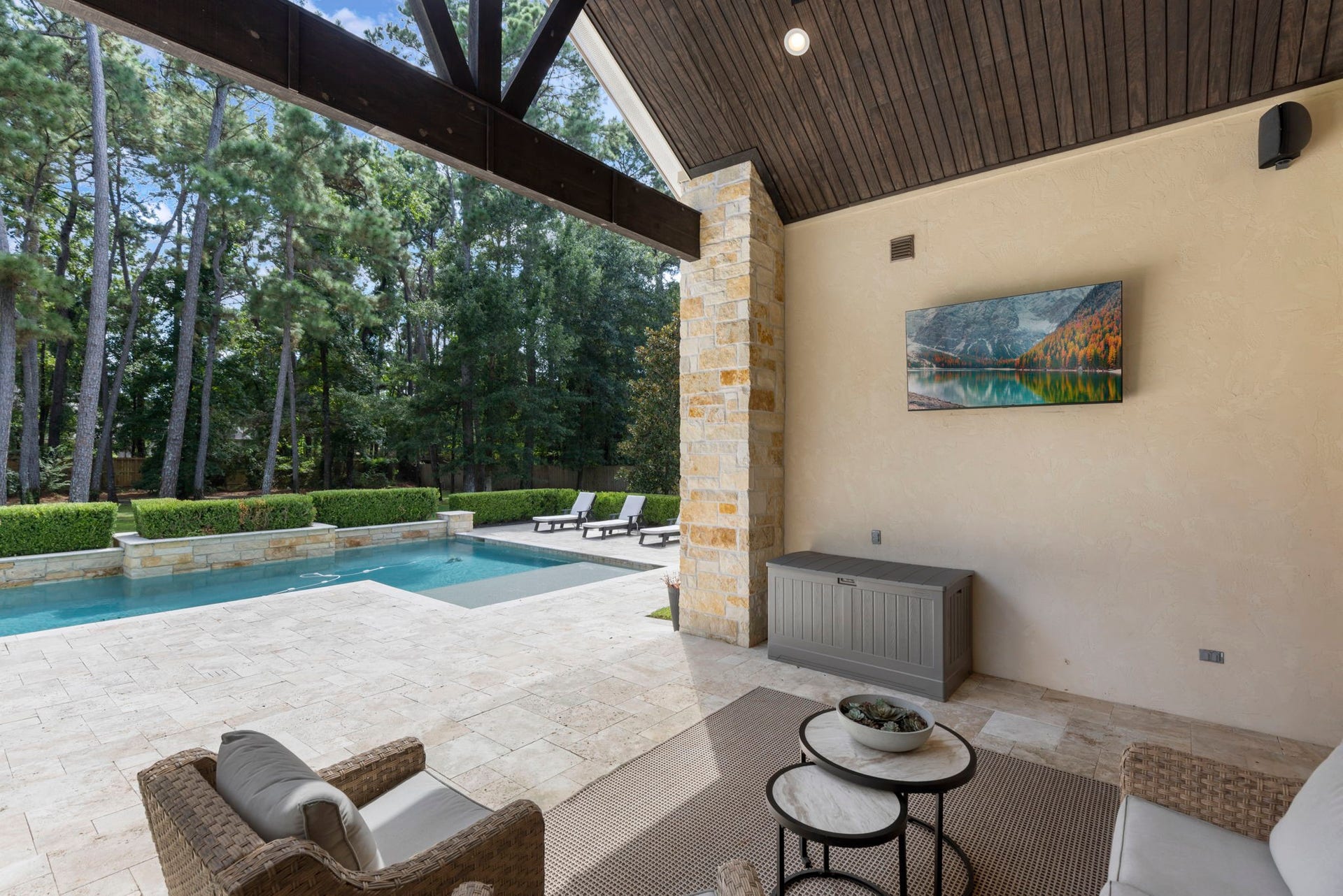 This angle showcases the patio's outdoor entertainment setup, with a mounted television and ample covered space for year-round enjoyment beside the pool.