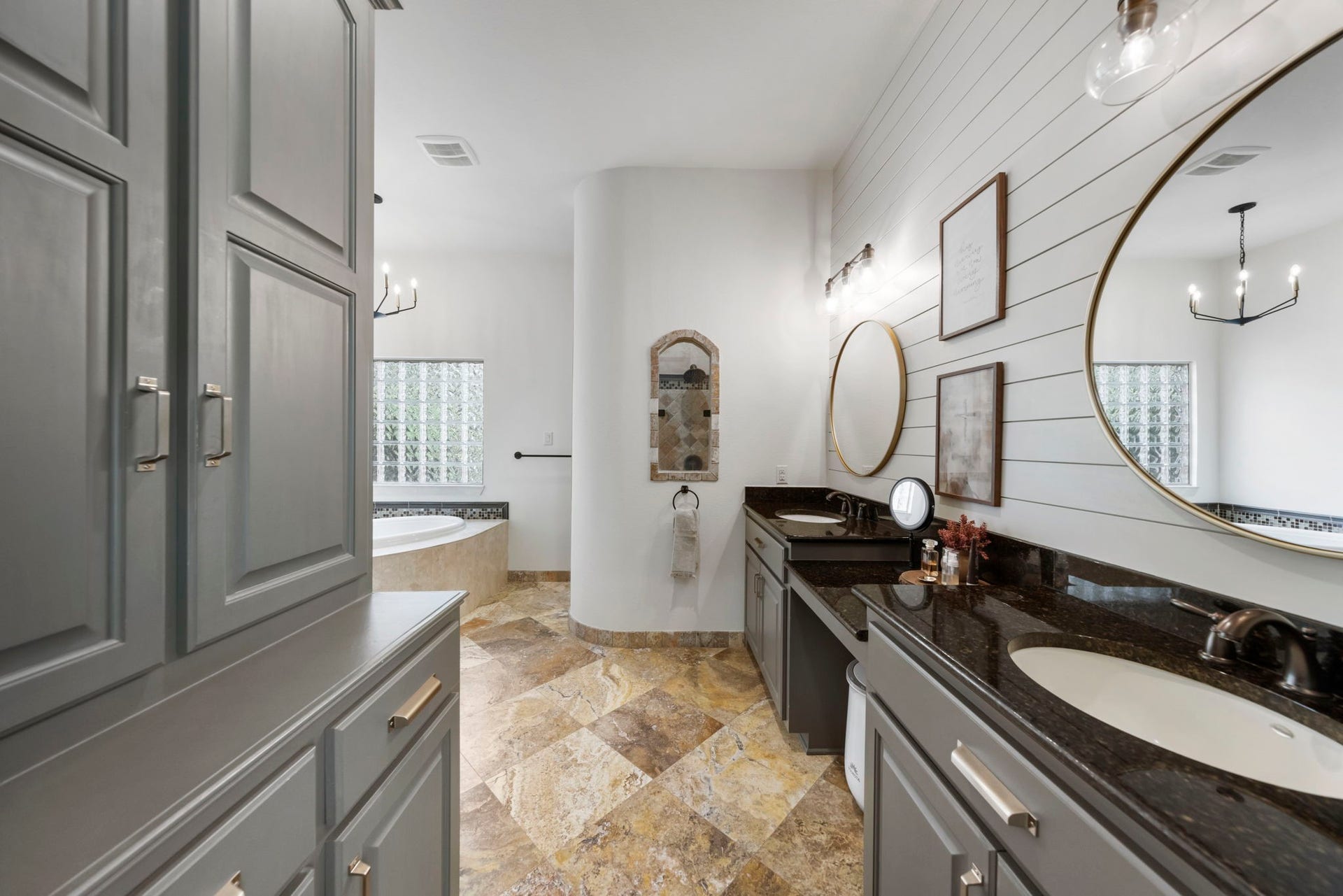 A spa-inspired retreat featuring warm travertine flooring in a striking diamond pattern, a corner soaking tub, and a sleek shiplap accent wall.
