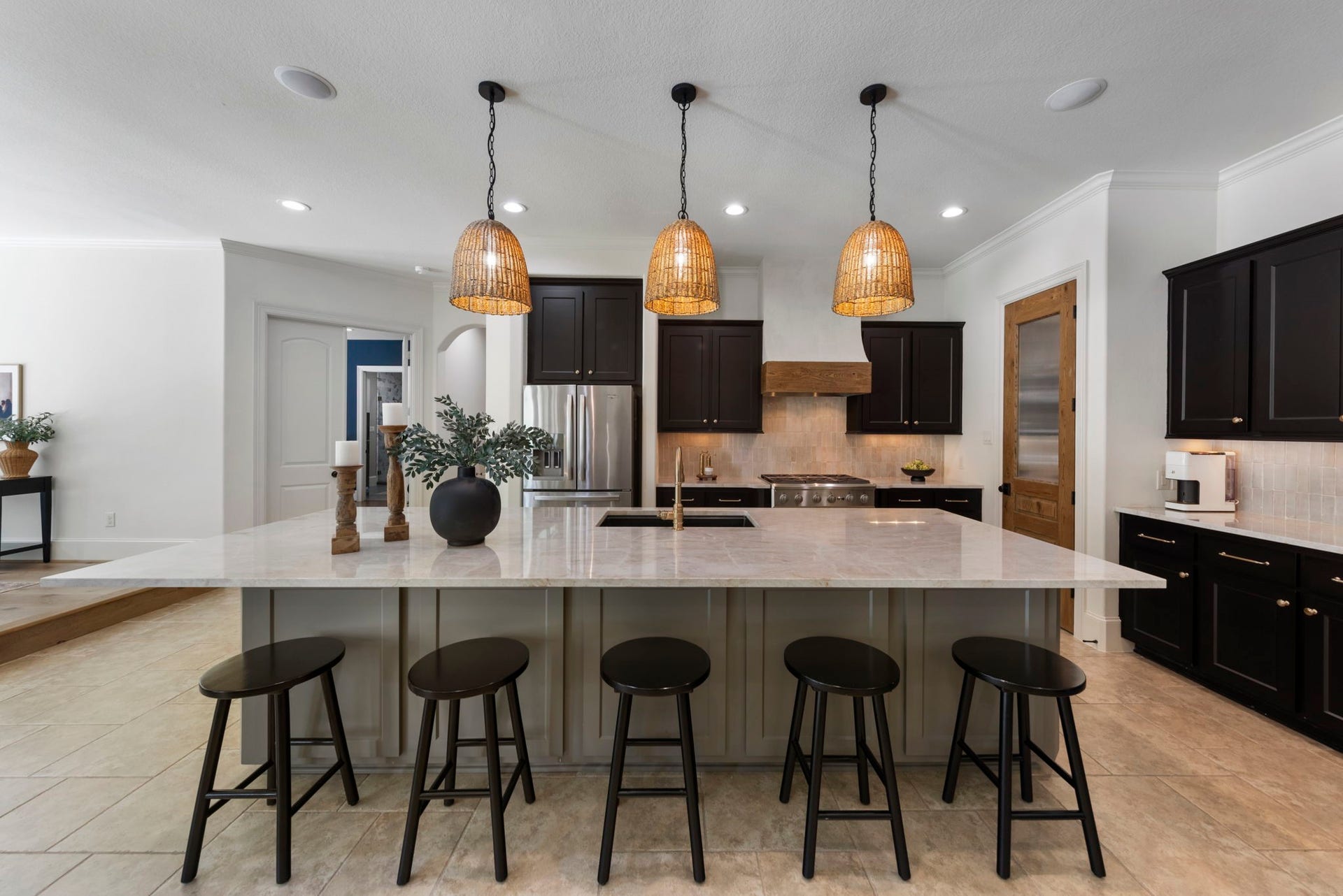 A show-stopping waterfall island wrapped in marble-look quartz anchors the chef's kitchen, illuminated by a trio of woven pendant lights. Espresso cabinetry and a designer brass faucet add sophisticated contrast.