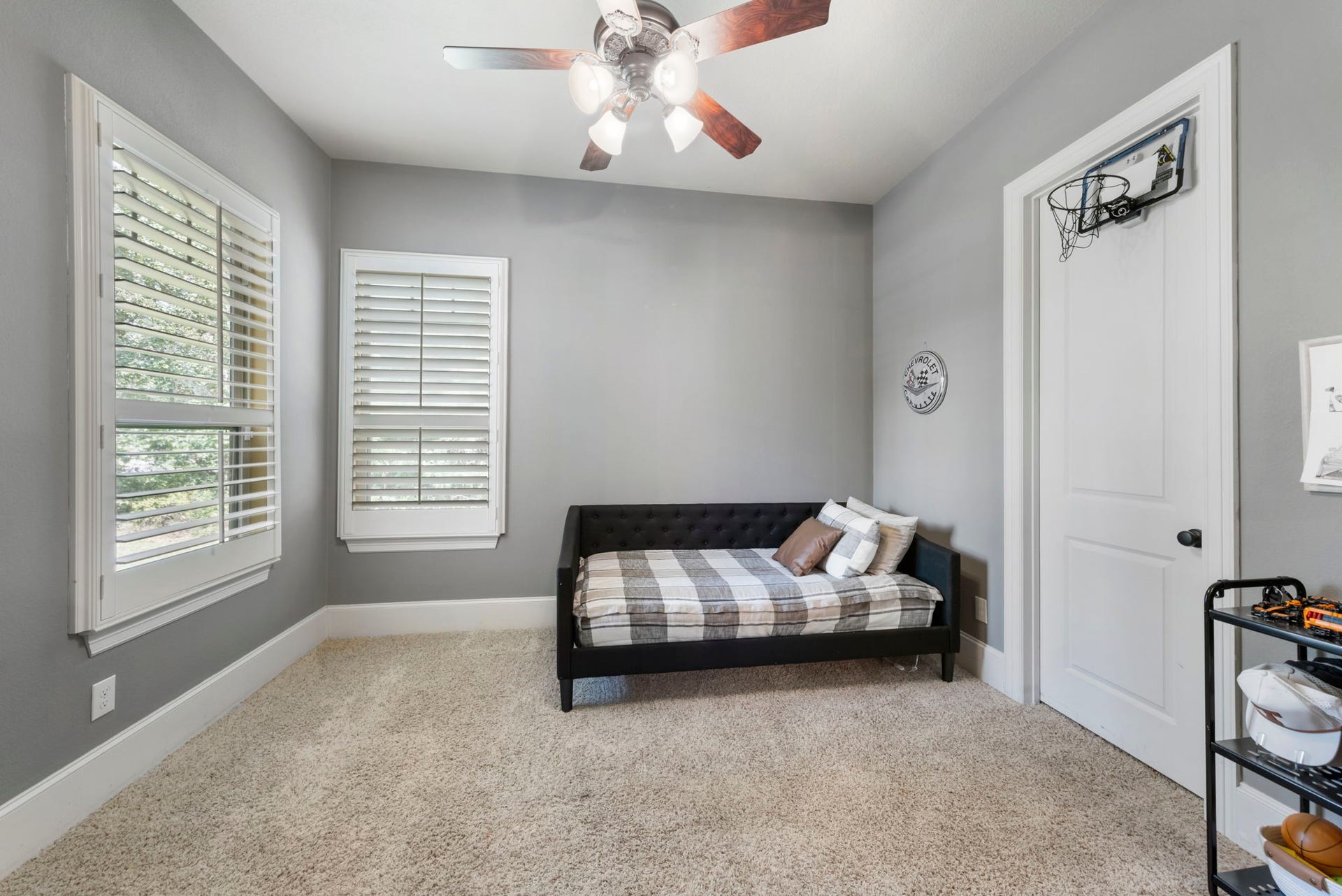 A versatile bedroom offers plush wall-to-wall carpet and generous window coverage dressed in plantation shutters, filling the space with soft natural light.