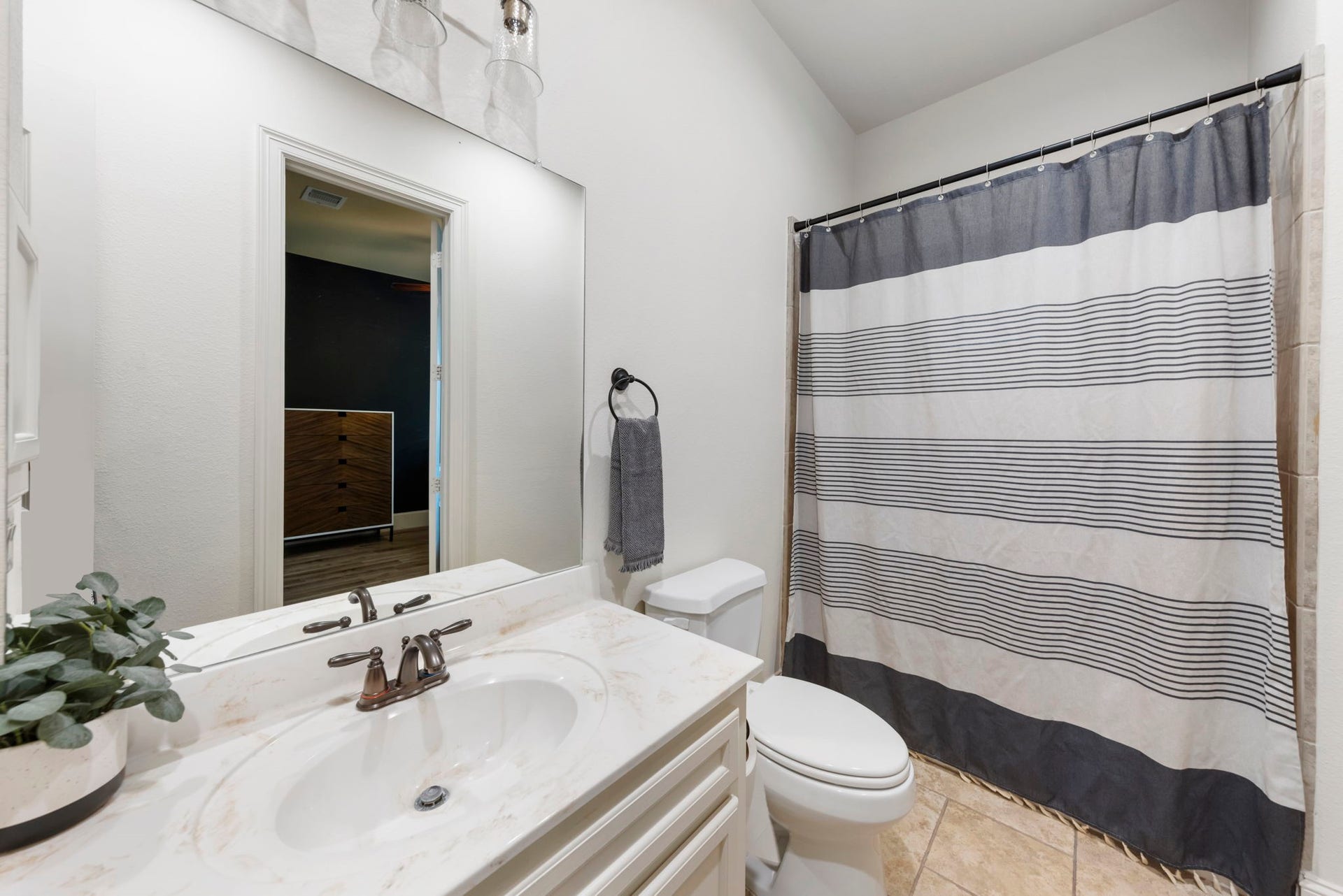 A crisp striped shower curtain and brass fixtures brighten this convenient en-suite, finished with a marble-look vanity top and warm tile flooring throughout.