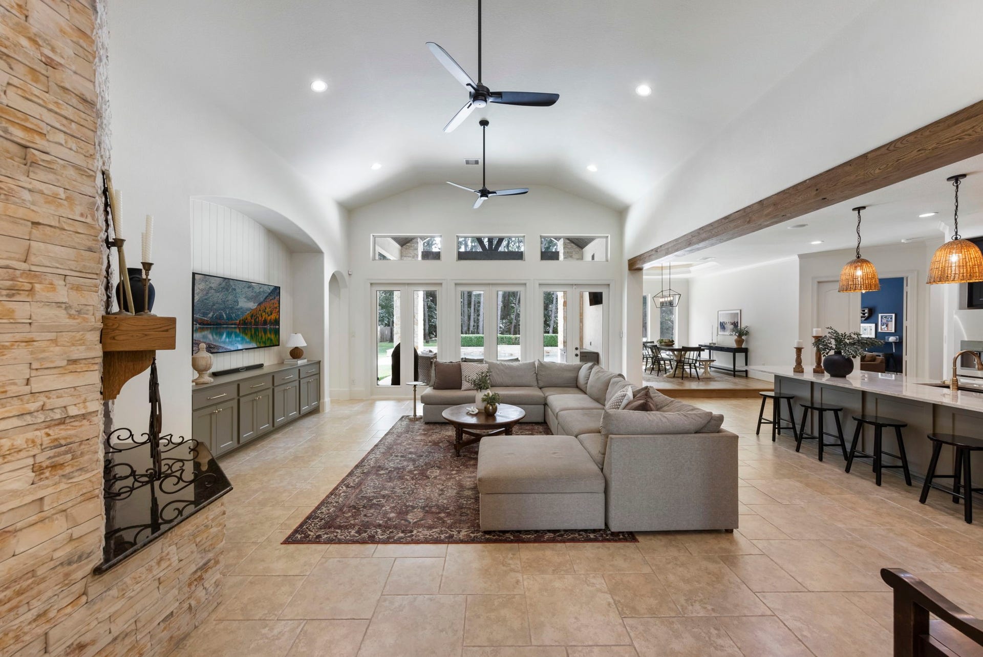 Soaring vaulted ceilings and dual modern fans crown an open-concept great room, with a wall of transom windows flooding the space with light. The layout flows effortlessly toward the gourmet kitchen beyond.