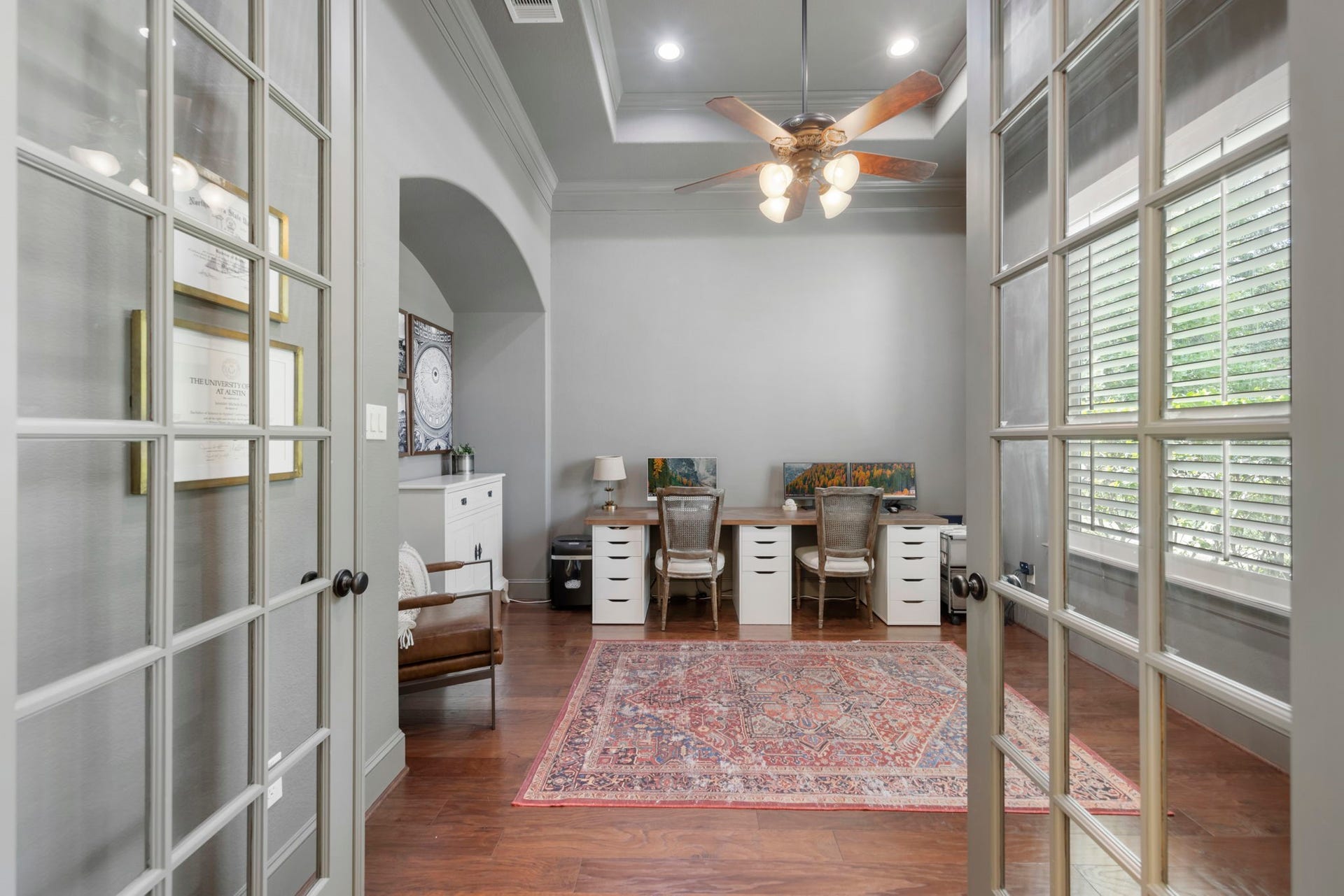 Tucked behind glass French doors, this sunlit study features tray-ceiling detailing, plantation shutters, and rich wood flooring underfoot. A private, quiet retreat ideal for working from home.