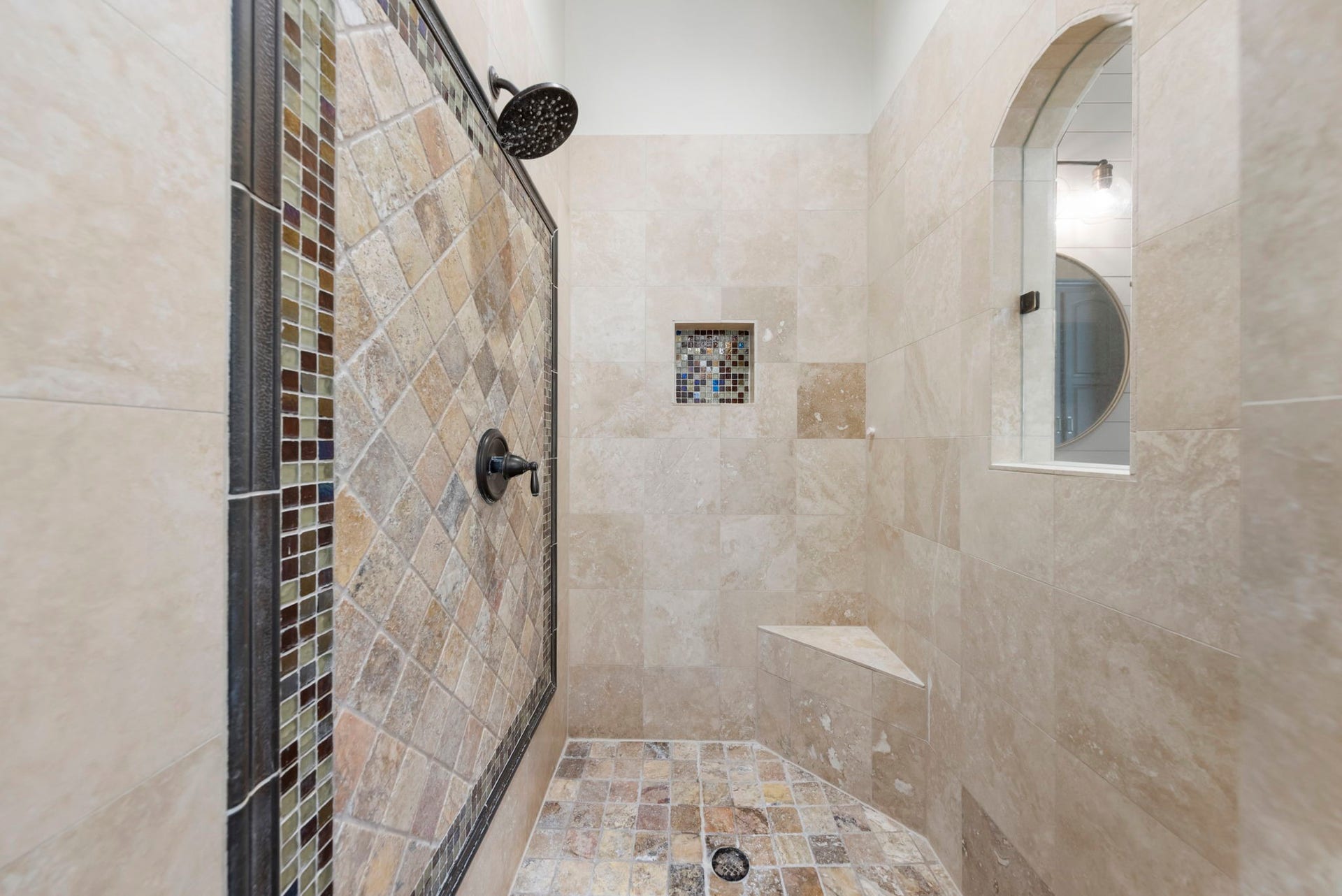 An oversized walk-in shower showcases hand-set mosaic tile, a glass-block window for privacy with natural light, and a built-in bench seat.