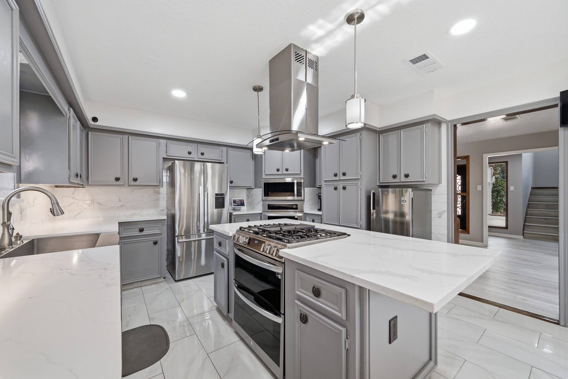 Beautifully updated kitchen with gray cabinetry, quartz countertops, stainless steel appliances, recessed lighting, and a center island.