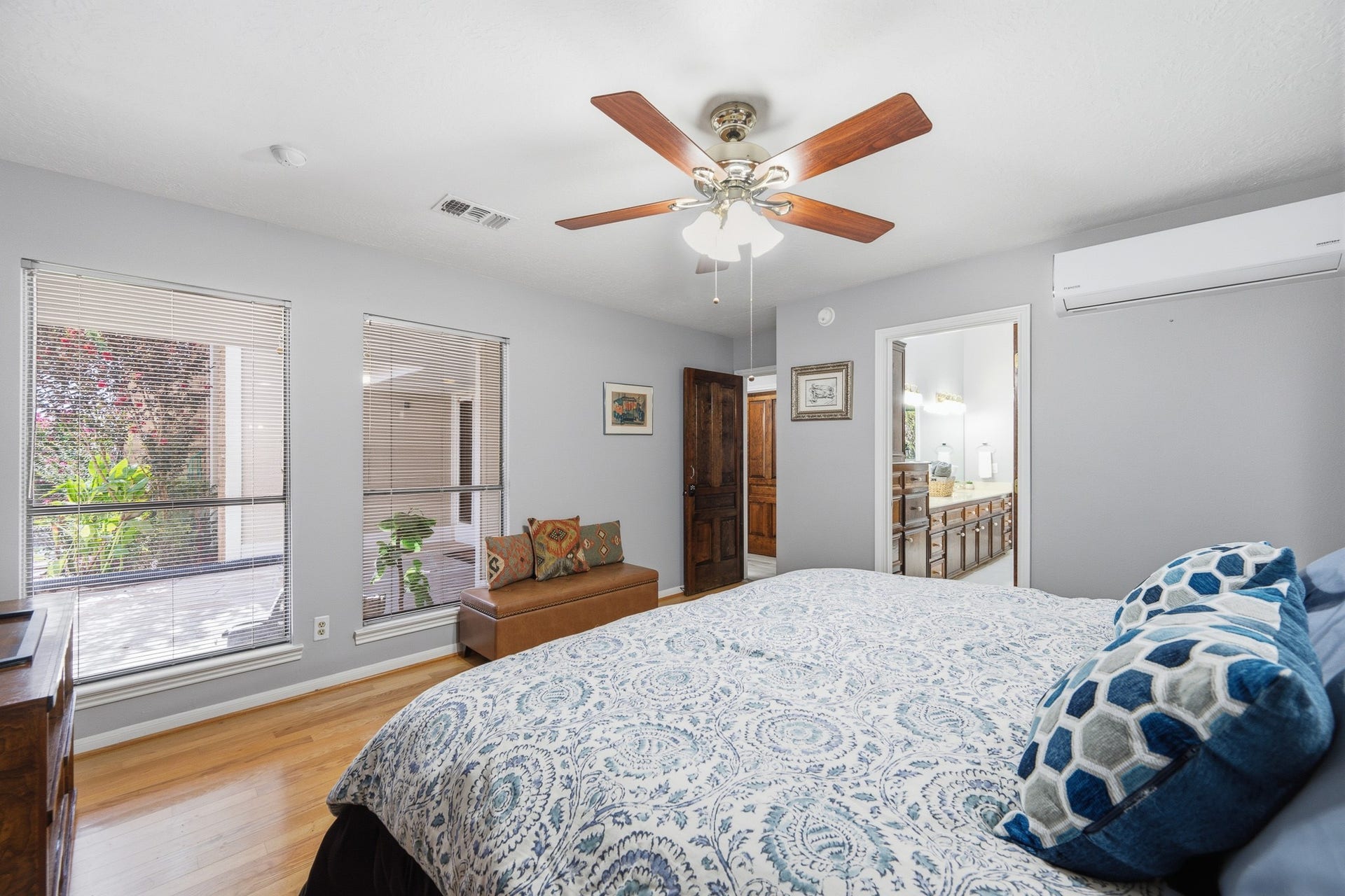 Spacious primary bedroom with wood flooring, a ceiling fan, and large wall of windows.