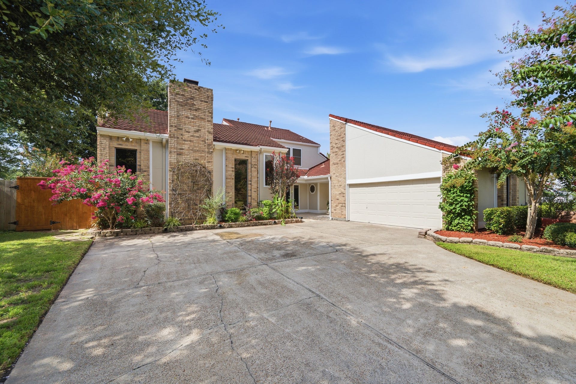 Welcoming front exterior with a wide driveway, mature landscaping, and an attached garage.