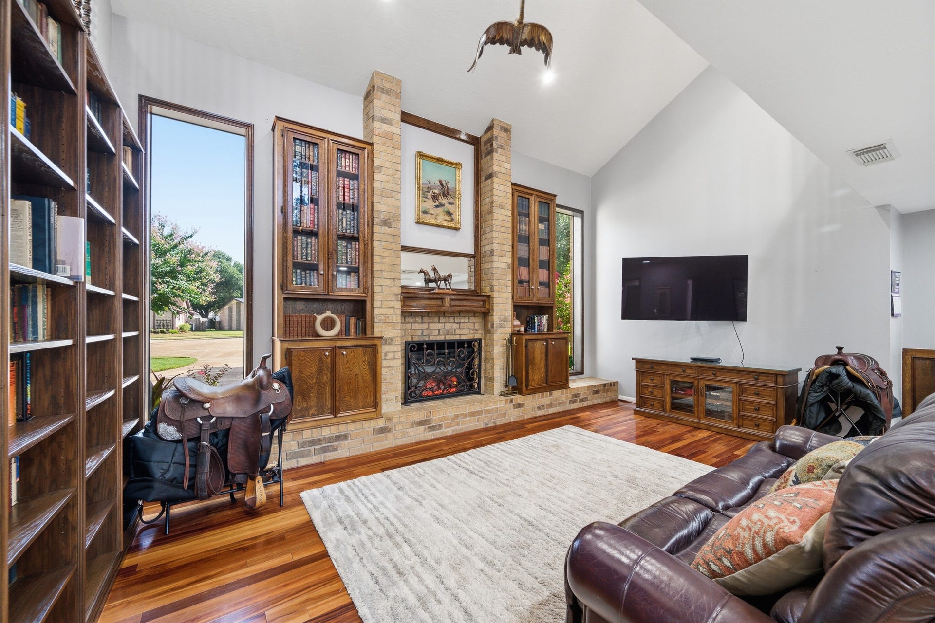 Dramatic living room with soaring ceilings, hardwood floors, custom built-ins, a fireplace, and abundant natural light.