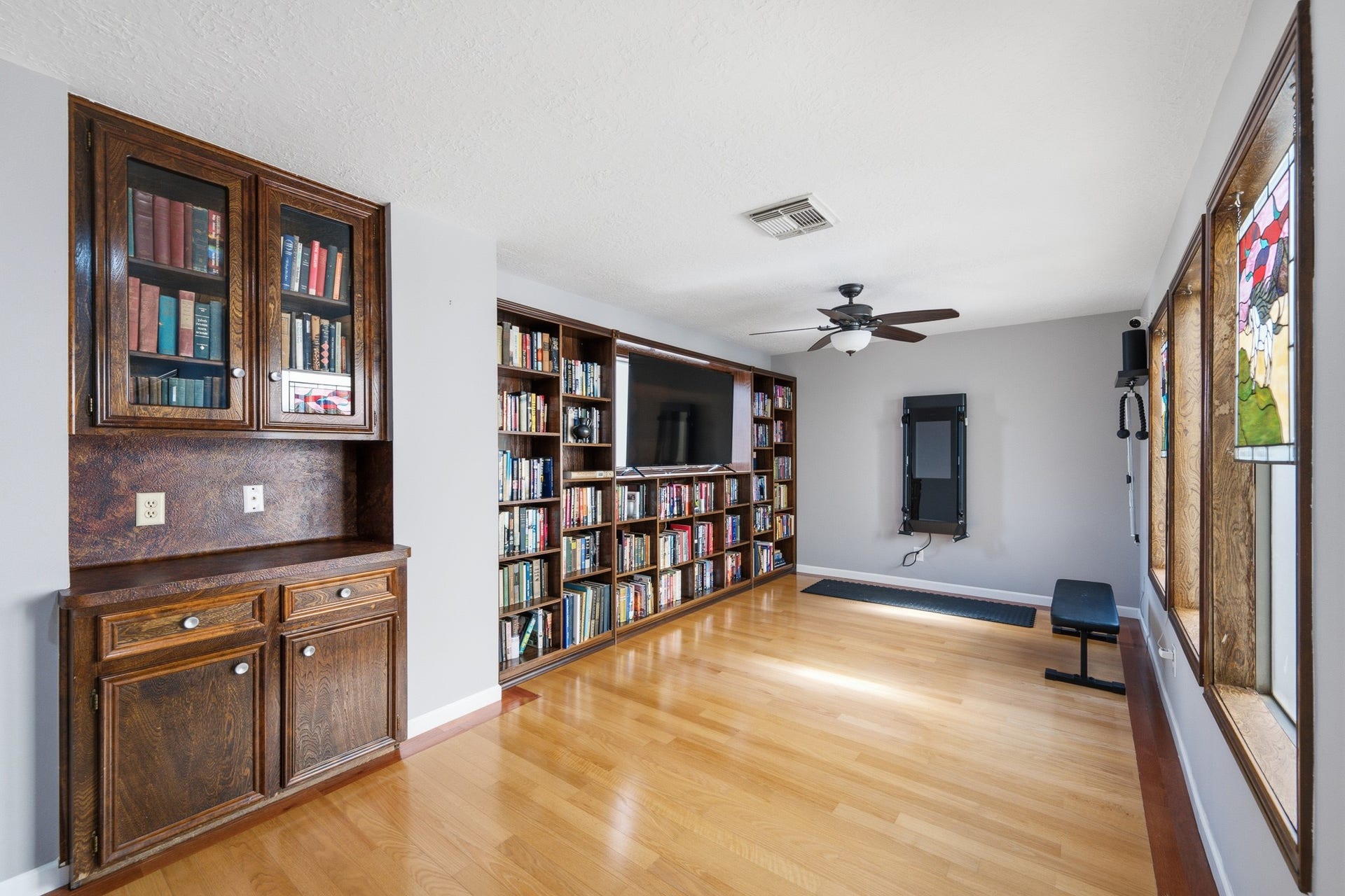 Versatile space with hardwood floors, built-in bookcases, cabinetry, and a wall of windows.