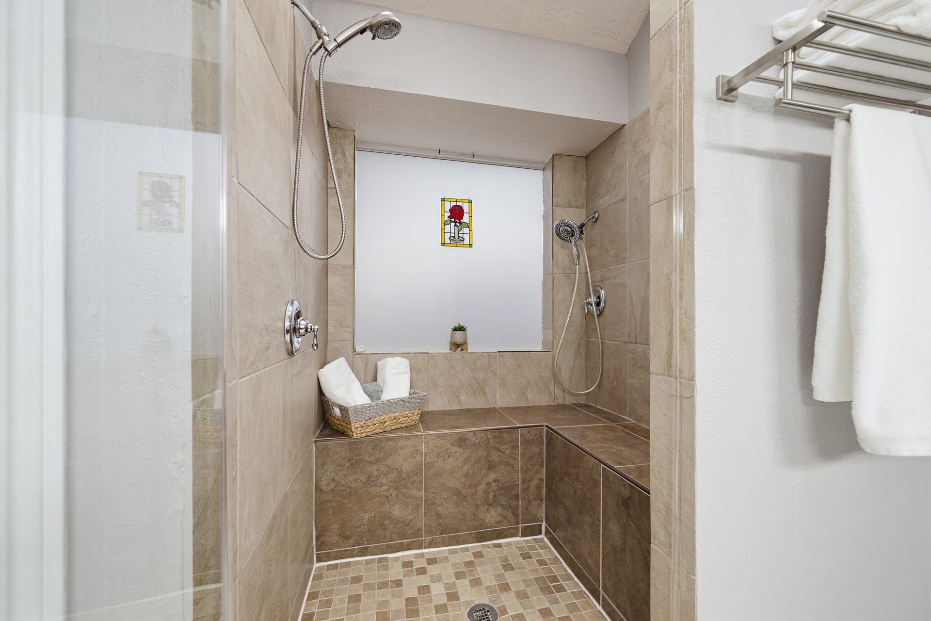 Oversized walk-in shower featuring tile surround, built-in seating, dual showerheads, and a handheld sprayer.