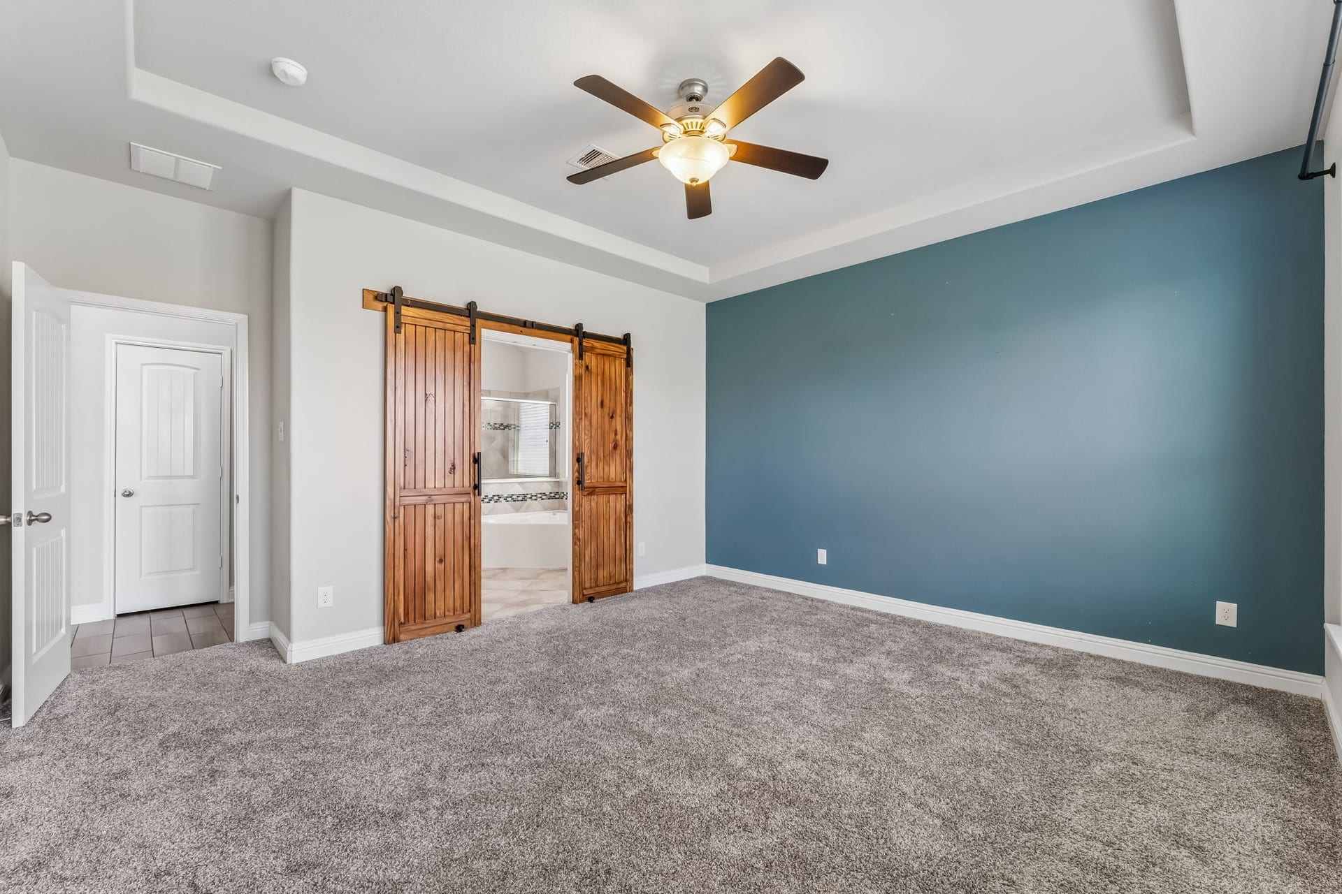 5107 Baroness Lane, Katy, TX 77493 Spacious bedroom featuring a cozy carpet, a striking blue accent wall, and elegant wooden barn doors leading to an en-suite bathroom.