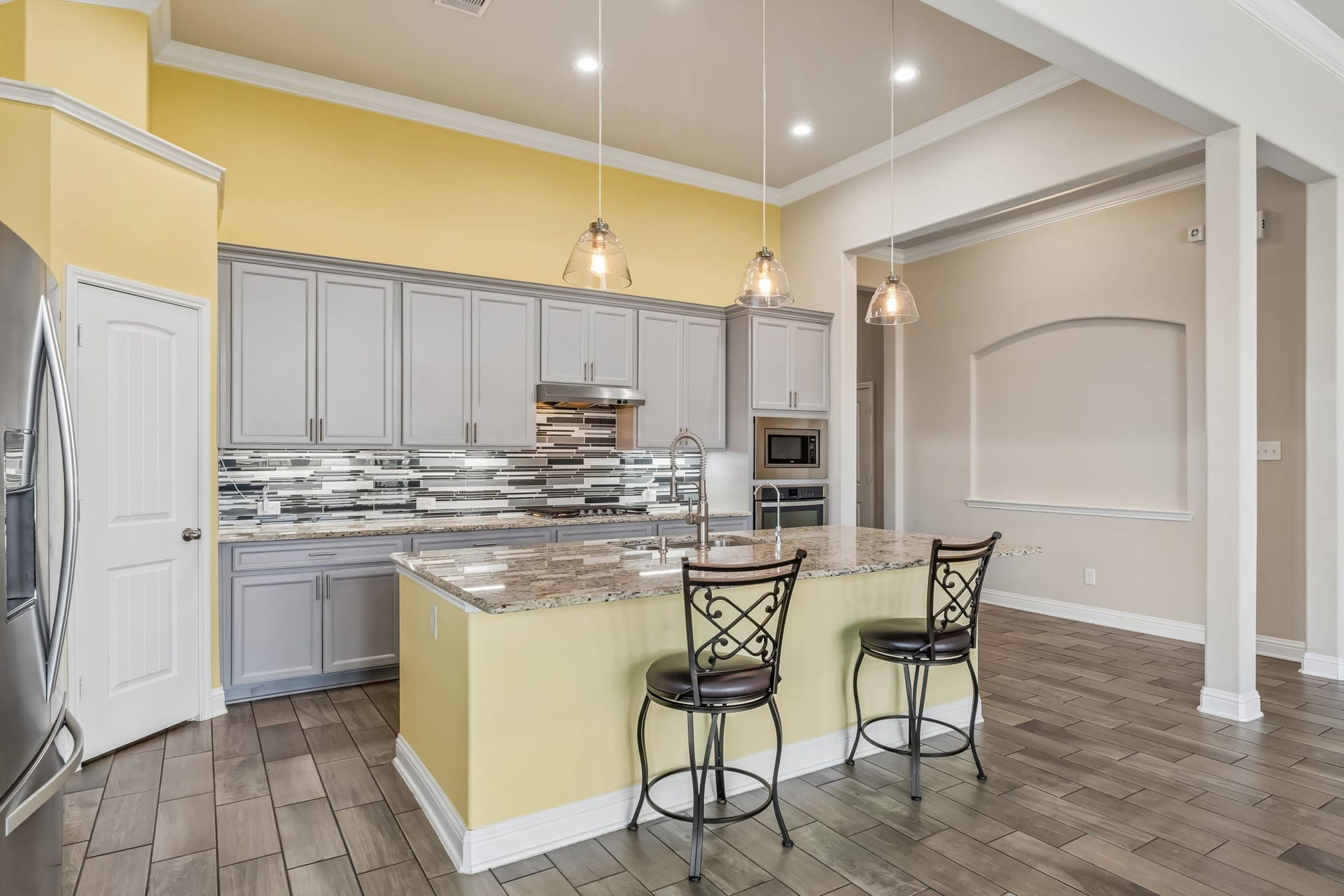5107 Baroness Lane, Katy, TX 77493 Bright and spacious kitchen featuring sleek gray cabinetry, a stylish tile backsplash, and a large granite island with seating.