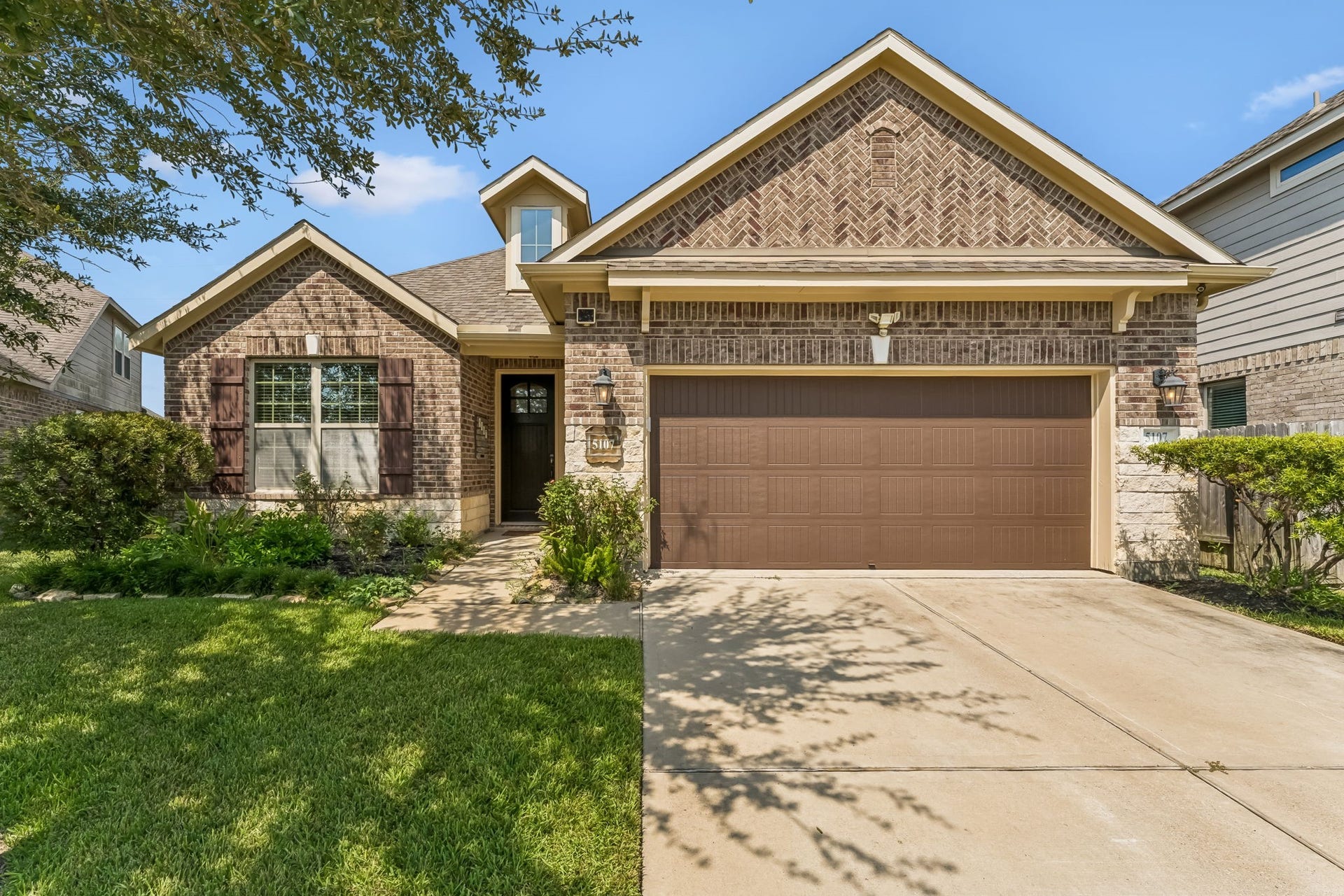 5107 Baroness Lane, Katy, TX 77493 Charming brick home with a welcoming front porch, neatly manicured lawn, and a spacious two-car garage.