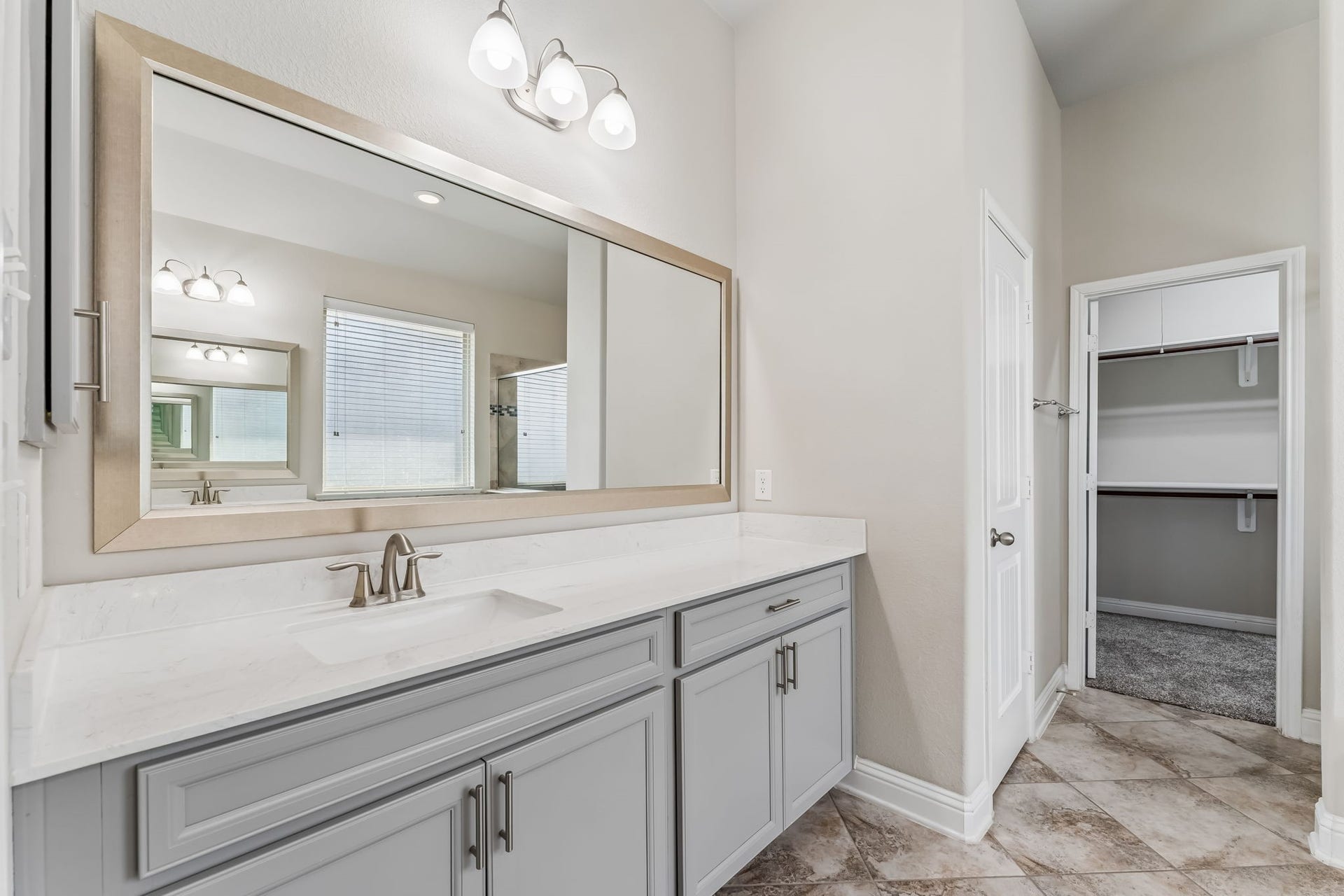 5107 Baroness Lane, Katy, TX 77493 Elegant bathroom featuring a spacious vanity with a sleek countertop, large mirror, and modern lighting, leading into a roomy walk-in closet.