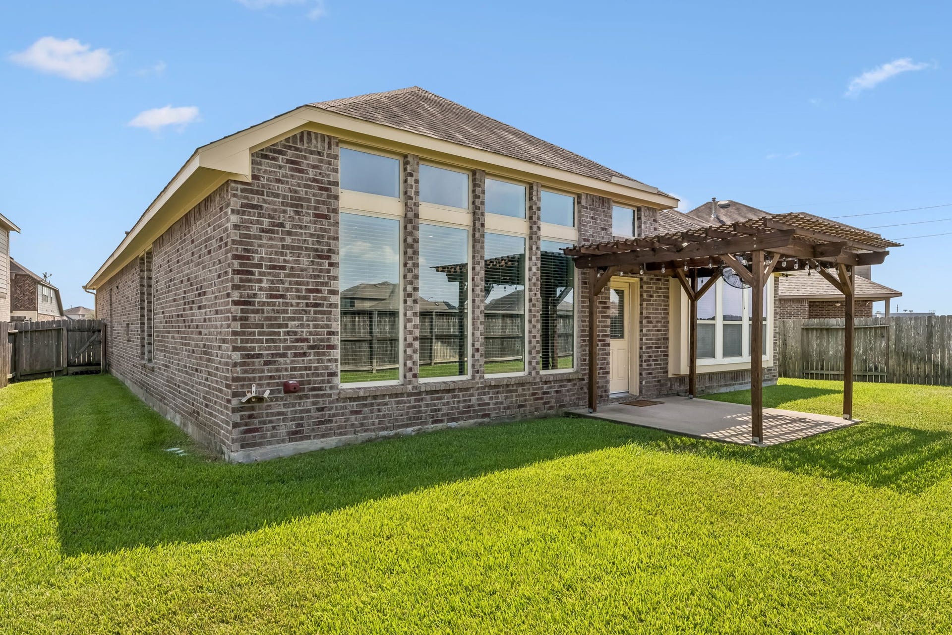 5107 Baroness Lane, Katy, TX 77493 Charming brick home with large windows and a cozy pergola-covered patio, set in a spacious, well-maintained backyard.