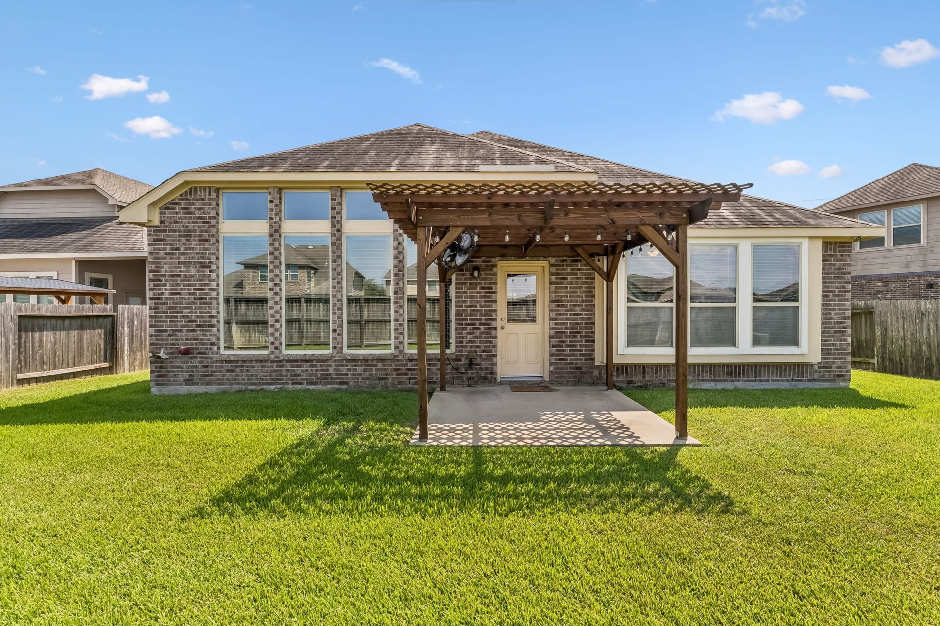 5107 Baroness Lane, Katy, TX 77493 Charming brick exterior with large windows and a cozy pergola-covered patio, perfect for outdoor relaxation in the spacious backyard.