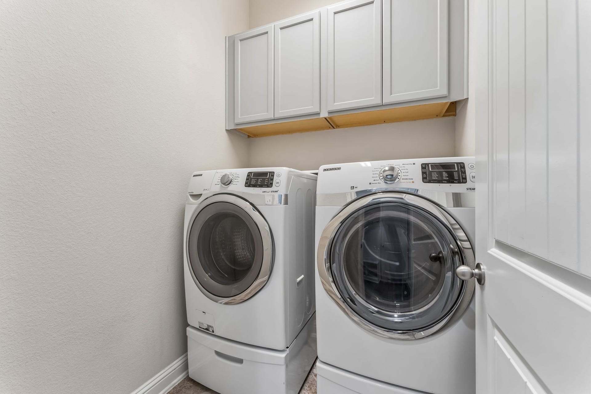5107 Baroness Lane, Katy, TX 77493 Modern laundry room featuring a high-efficiency washer and dryer set, complemented by ample overhead storage cabinets.