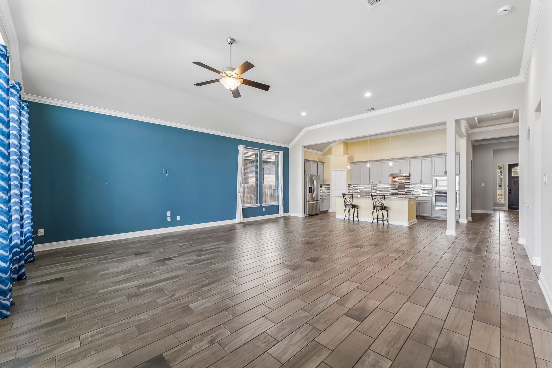 5107 Baroness Lane, Katy, TX 77493 Spacious open-concept living area with sleek hardwood floors, a striking blue accent wall, and a modern kitchen featuring stainless steel appliances and a large island with bar seating.