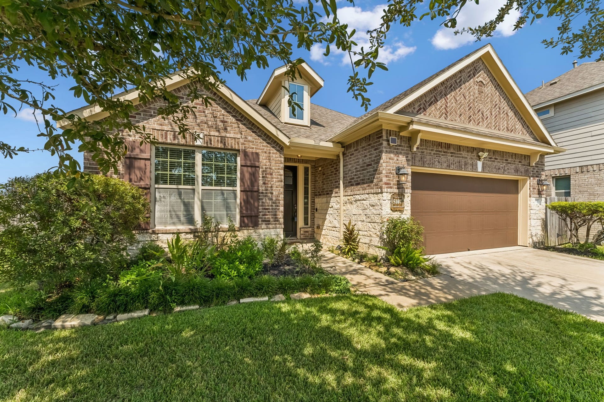5107 Baroness Lane, Katy, TX 77493 Charming brick home with a welcoming front porch and manicured landscaping, featuring a spacious two-car garage and a neatly maintained front yard.