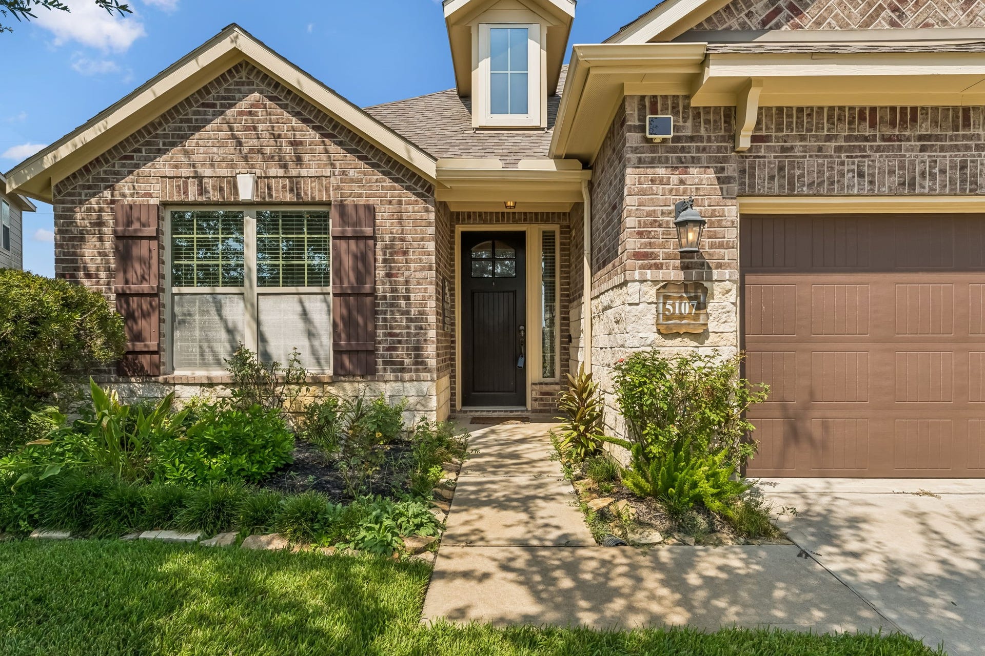 5107 Baroness Lane, Katy, TX 77493 Charming brick exterior with a welcoming front porch, accented by lush landscaping and a classic lantern light.