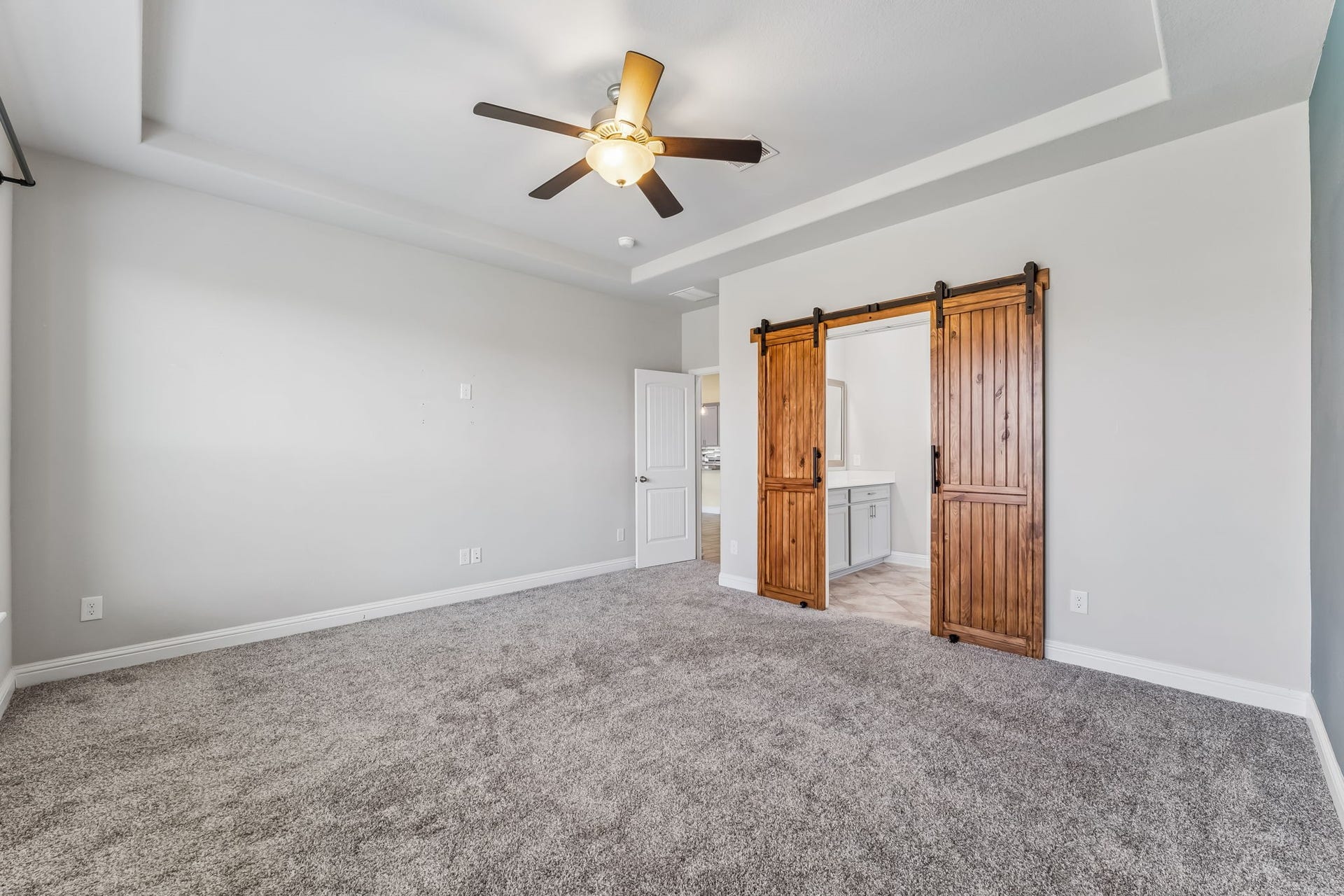 5107 Baroness Lane, Katy, TX 77493 Spacious bedroom with plush carpeting, featuring a ceiling fan and charming wooden barn doors leading to an en-suite bathroom.