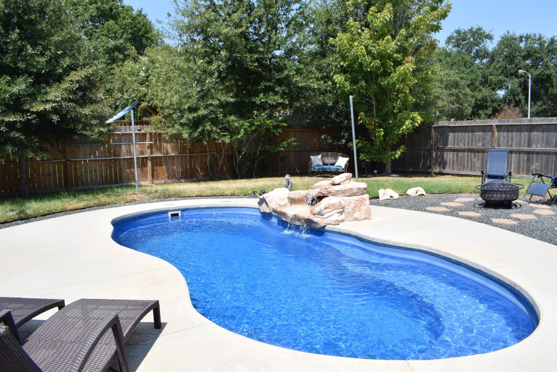 22510 Rangeview Drive, Katy, TX 77450 Experience relaxation in a charming backyard oasis featuring a sparkling pool with a cascading waterfall, surrounded by lush greenery and ample seating for outdoor enjoyment.