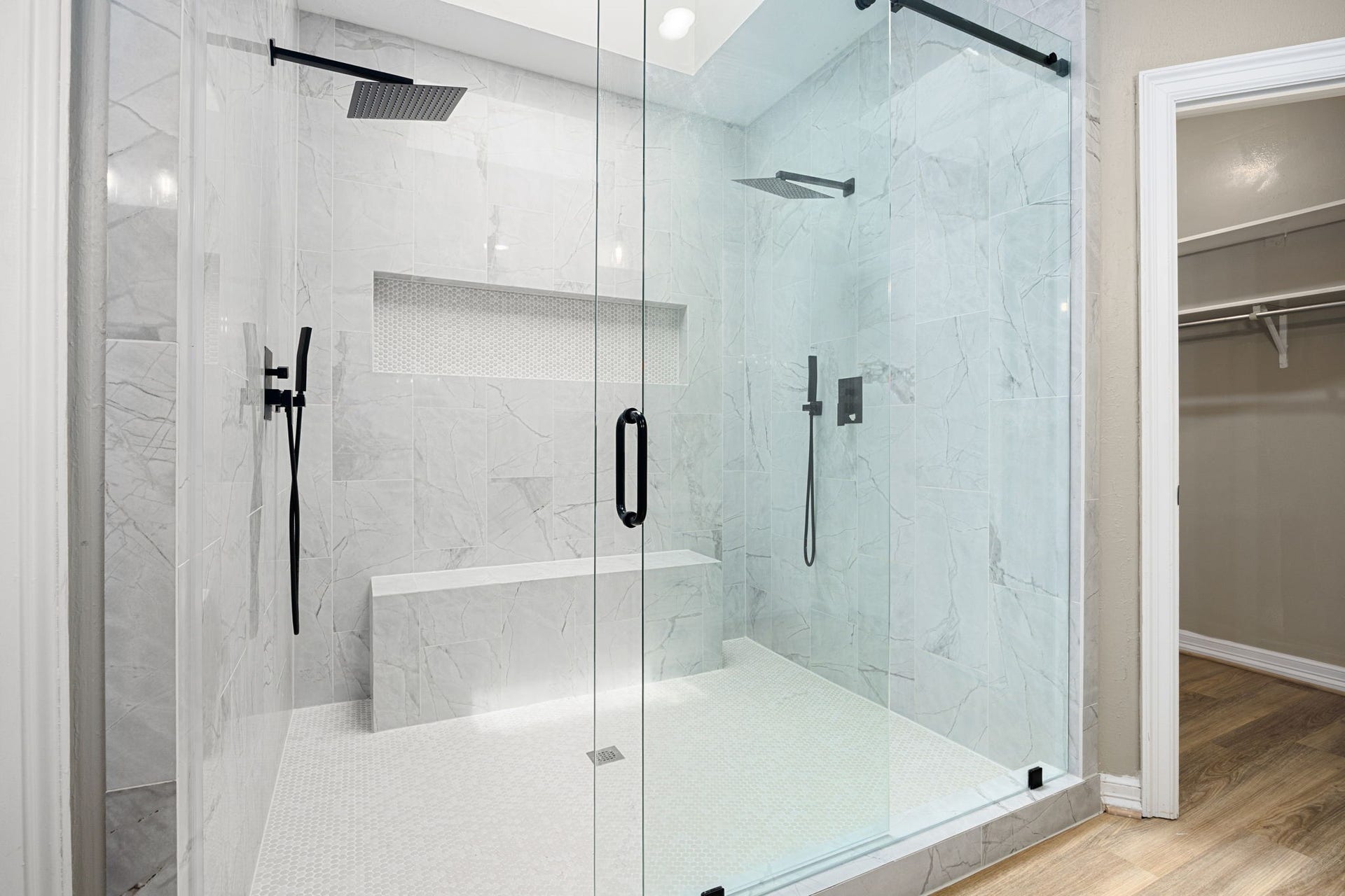 Oversized walk-in shower with elegant, frameless glass enclosure featuring a skylight and surrounded by two walk-in closets.