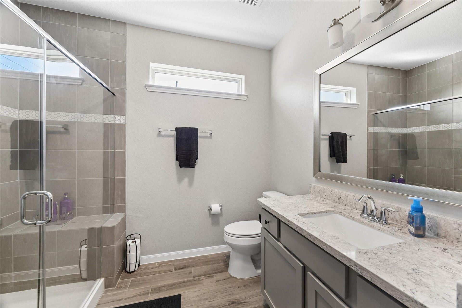 14918 Lake Shore Avenue, Mont Belvieu, TX 77523 Located in the downstairs guest wing, this secondary full bathroom serves the nearby bedroom and additional living space, with a tub-and-shower combination, wide mirror, and vanity storage.