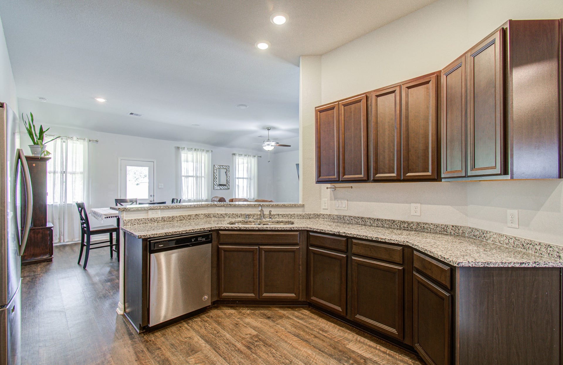 11064 Patriot Court, Cleveland, TX 77328 Spacious kitchen with elegant dark wood cabinetry, granite countertops, and stainless steel appliances, seamlessly flowing into a bright, airy dining area with large windows.