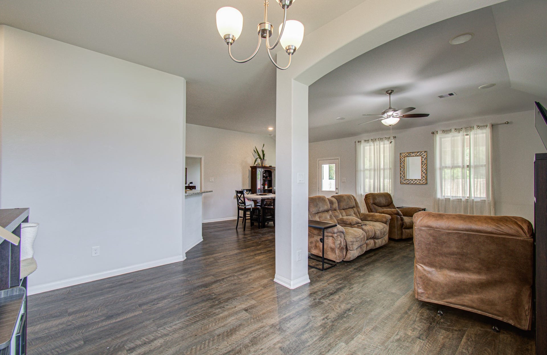 11064 Patriot Court, Cleveland, TX 77328 Spacious living area with elegant with wood-like floors, featuring a cozy seating arrangement and abundant natural light from large windows. A ceiling fan adds comfort, while an open archway leads to the dining space.