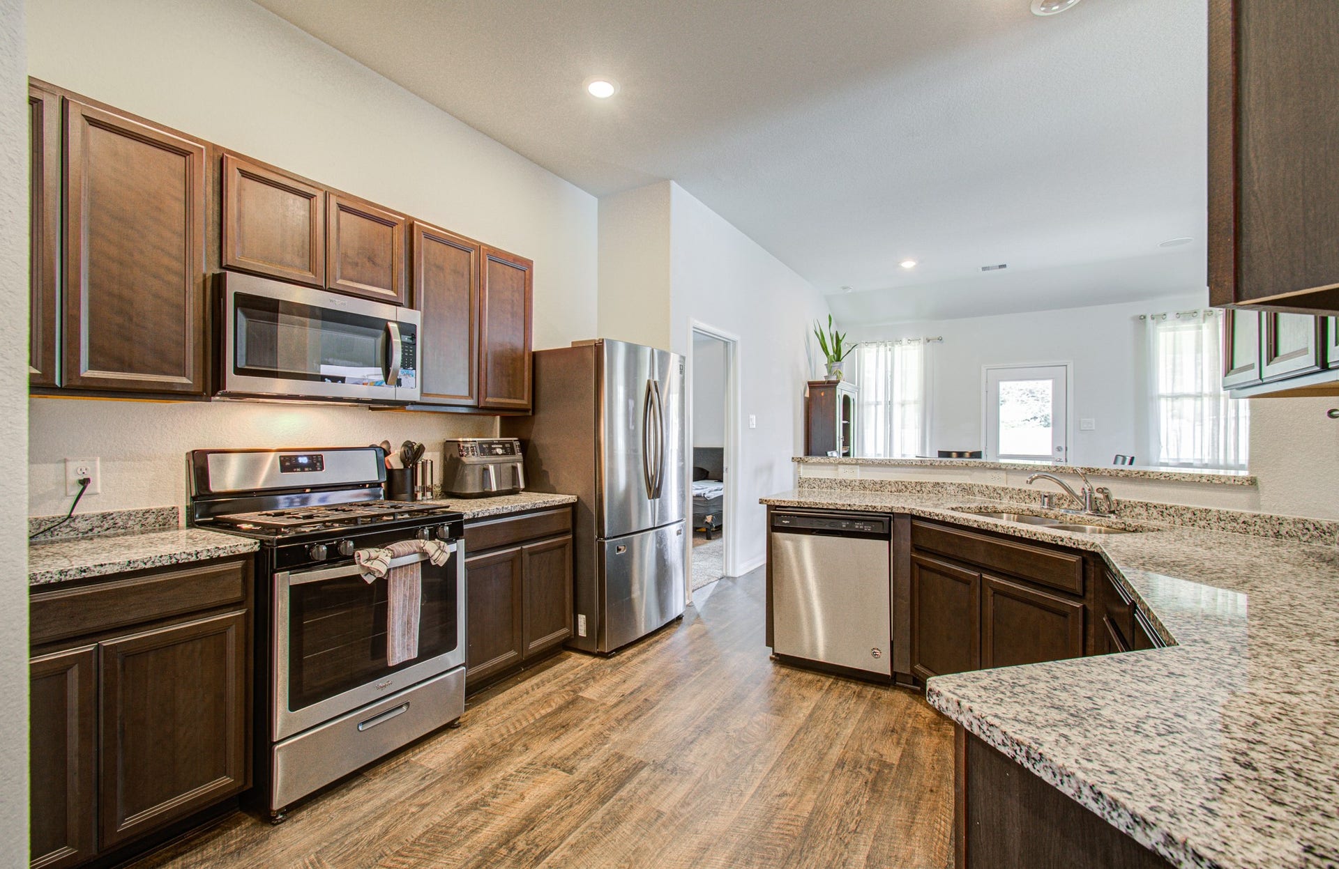 11064 Patriot Court, Cleveland, TX 77328 Modern kitchen featuring sleek stainless steel appliances, elegant dark wood cabinetry, and expansive granite countertops, complemented by warm wood flooring and an open layout.